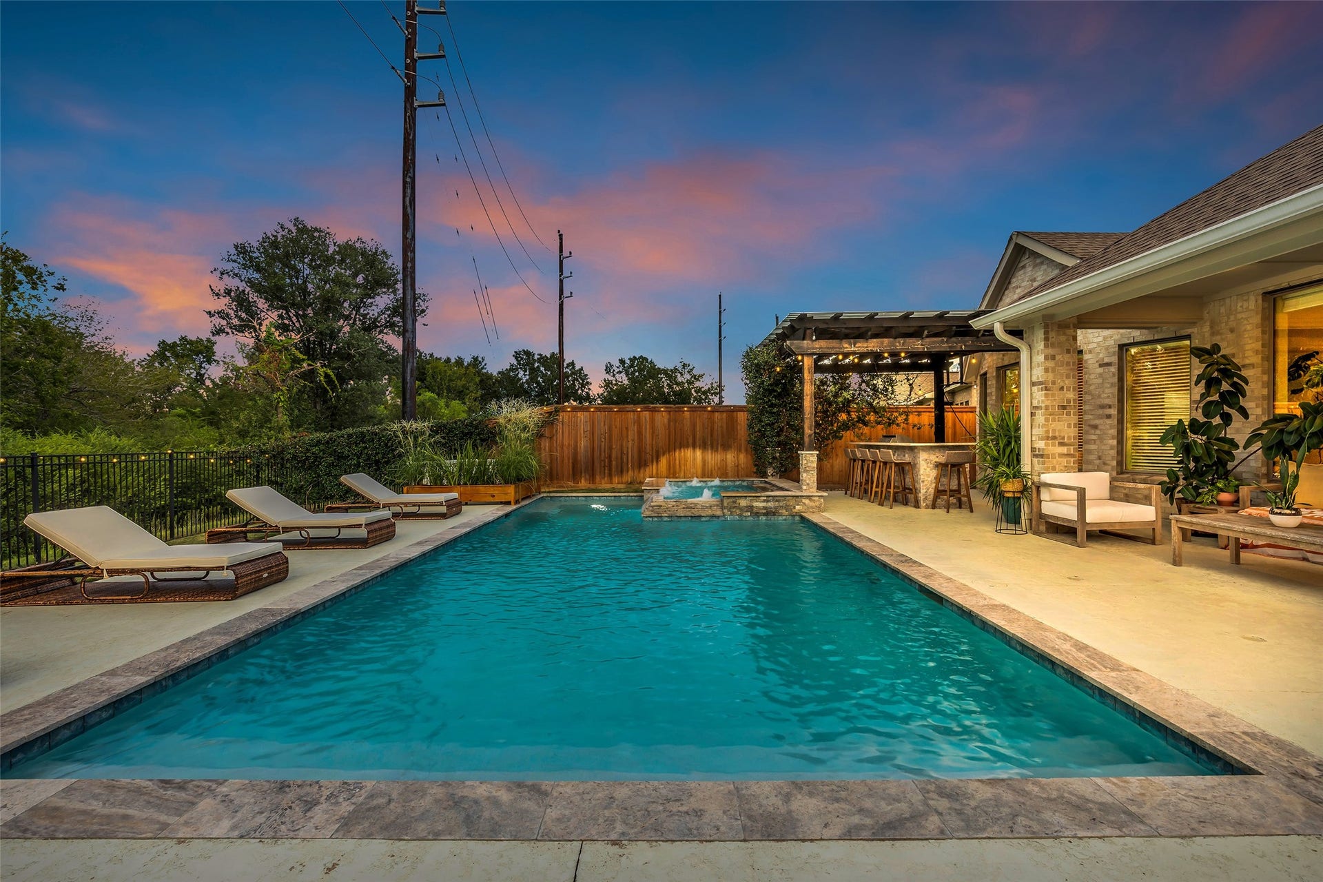 A long, rectangular pool with a spa and lounge deck, framed by mature trees and a privacy fence.