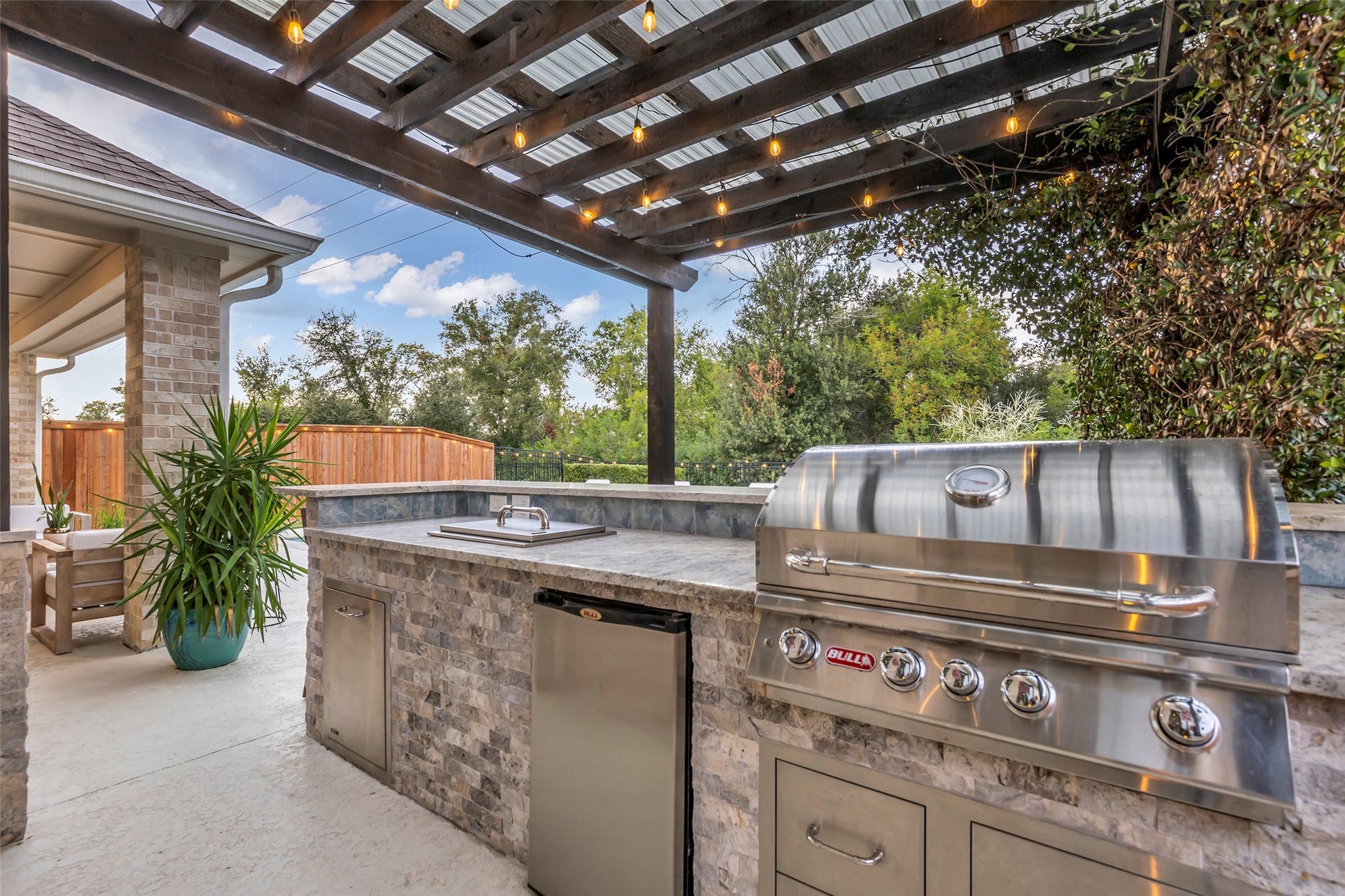Entertain in style with a stone-accented outdoor kitchen, built-in grill and mini fridge beneath a poolside pergola.