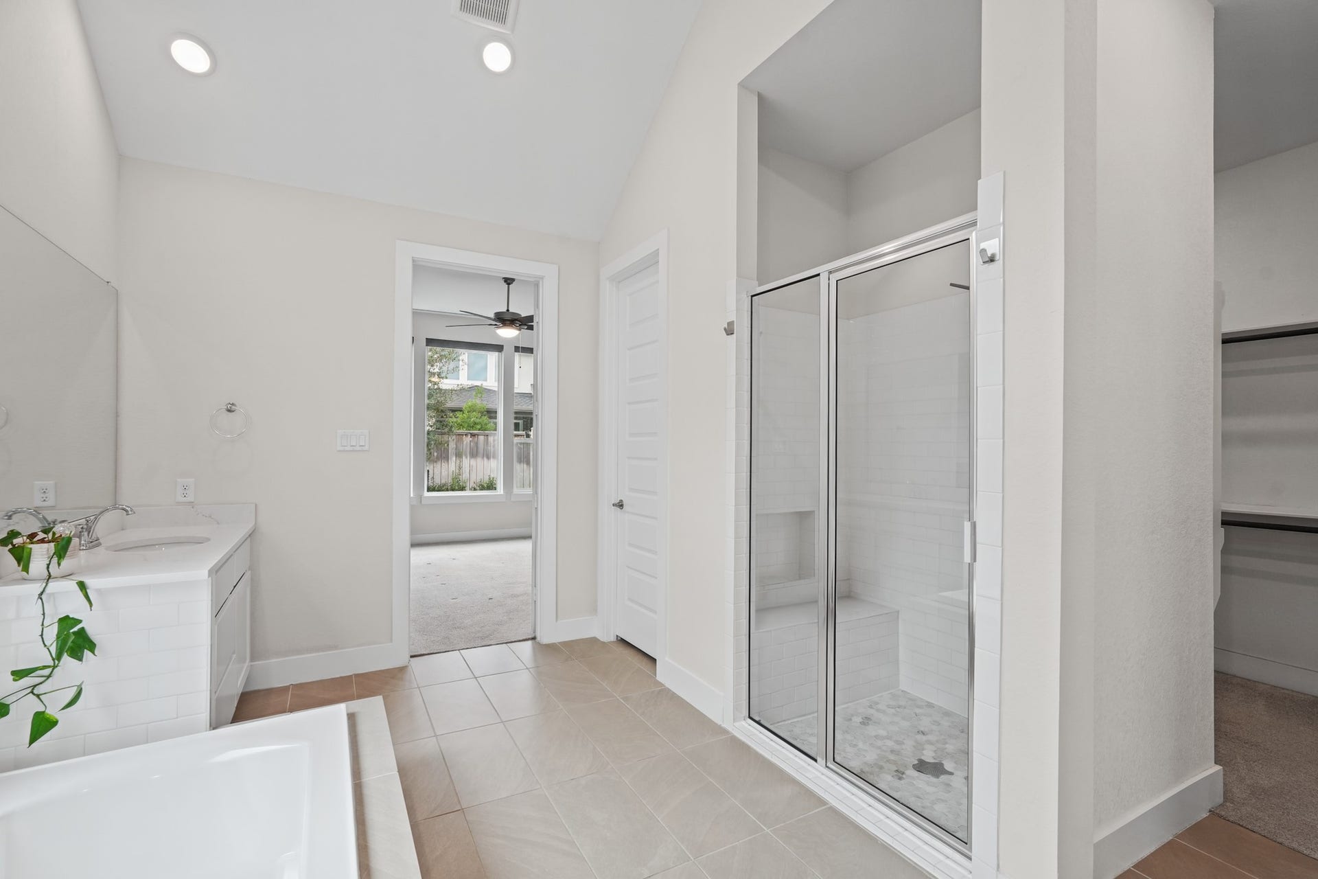A frameless glass shower and an extended vanity anchor the primary bath, with bright natural light and a neutral finish palette that keeps the space calm and uncluttered.