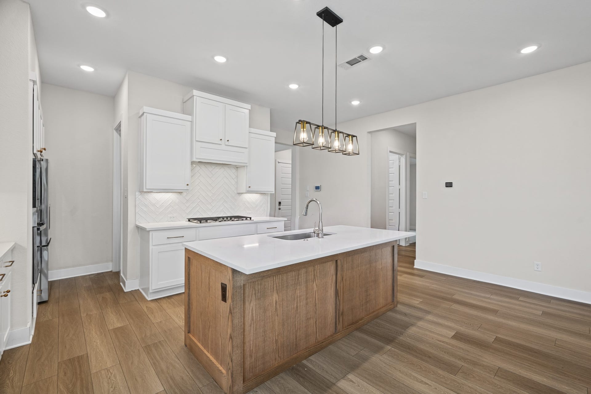 Wide-plank flooring carries from the entry through the kitchen, where the island, pendant lighting and full-height cabinetry keep the space bright, open and uncluttered.