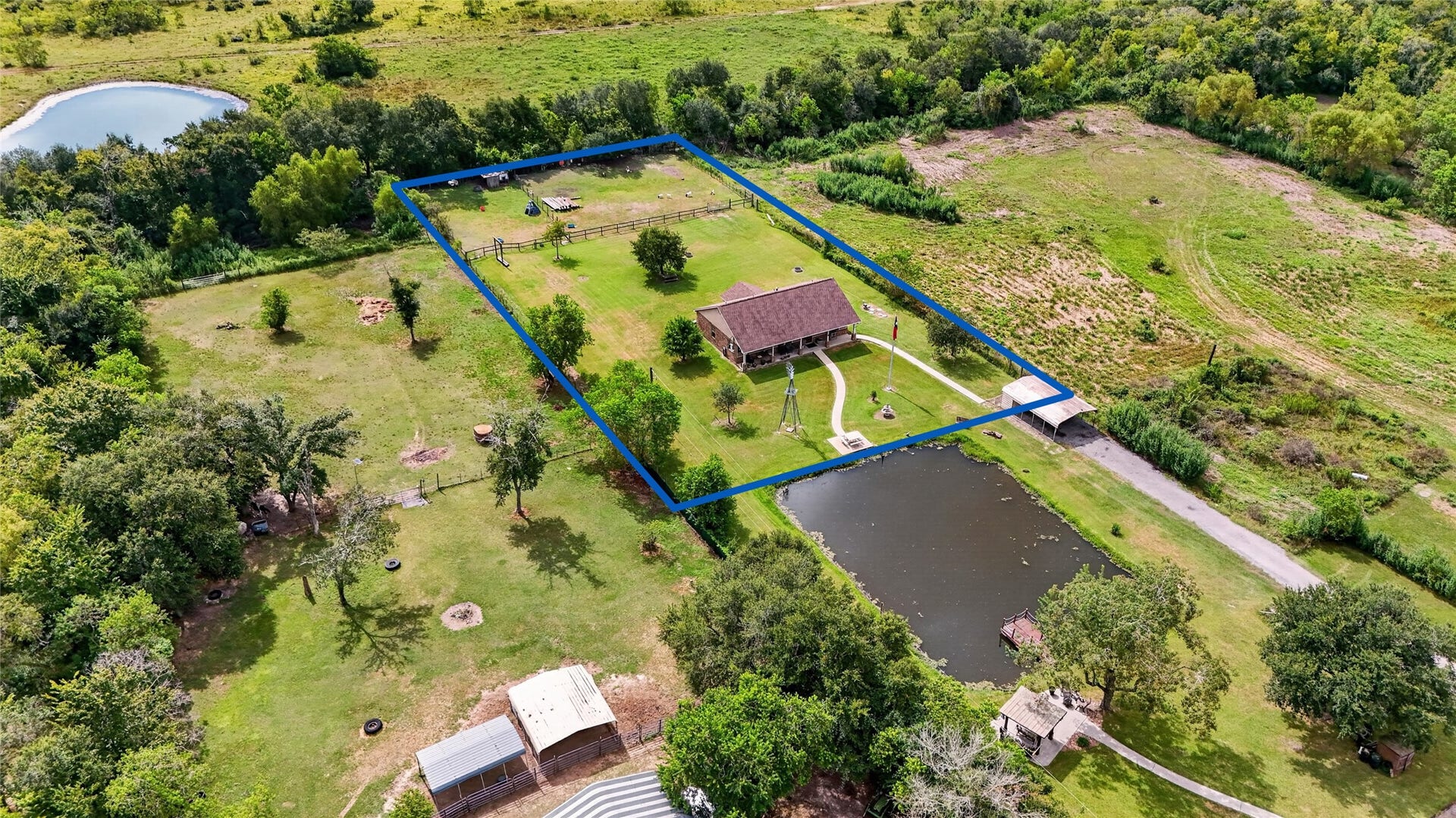 4933 1/2 Powers Ln, Alvin, TX 77511 Aerial view showcasing the property boundaries, expansive grounds, mature trees, fenced areas, and neighboring pond views.