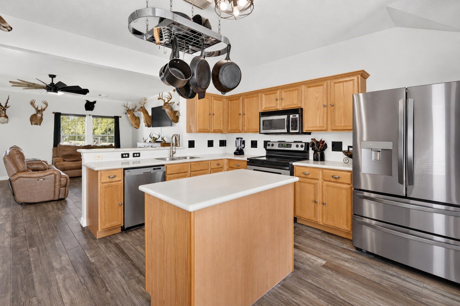 4933 1/2 Powers Ln, Alvin, TX 77511 Bright kitchen with a generous island, Corian countertops, hanging pot rack, and an open view into the living area.