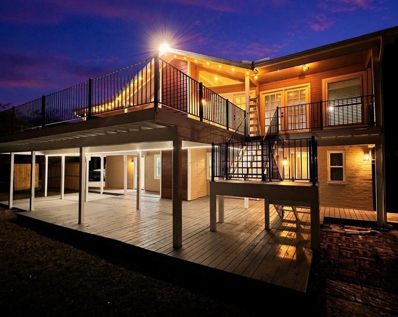 4509 Country Club Drive, Dickinson, TX 77539 Expansive upper and lower decks, modern railings, and warm exterior lighting that creates an inviting glow at dusk.