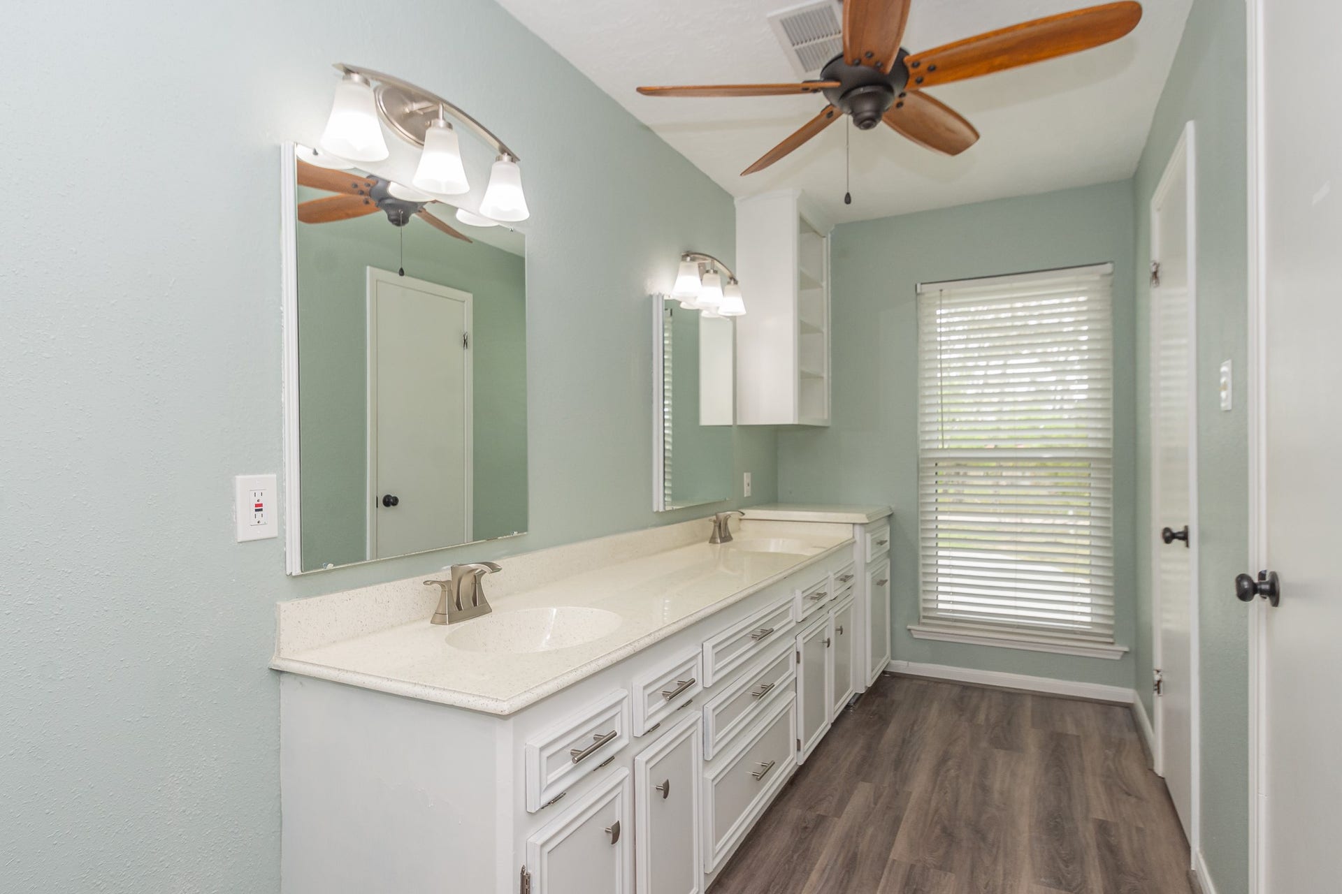 4509 Country Club Drive, Dickinson, TX 77539 Primary bathroom with a long dual-sink vanity and bright lighting. One door leading to the toilet and stand-up shower, the other into a walk-in closet.