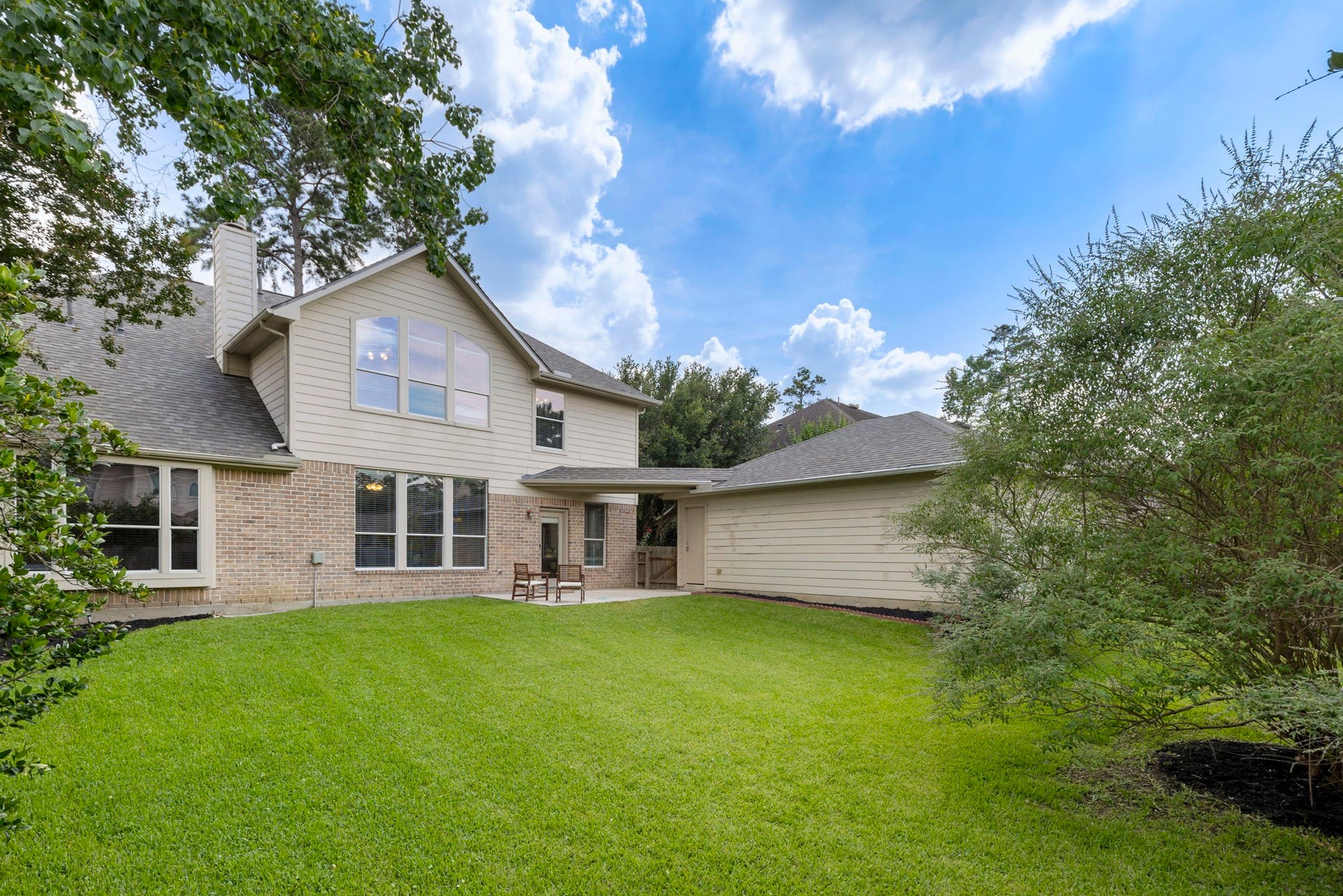 14 N Bardsbrook Circle, The Woodlands, TX 77382 A beautiful view of the home showcasing the generous backyard space, mature greenery, and large windows that bring natural light into the home.