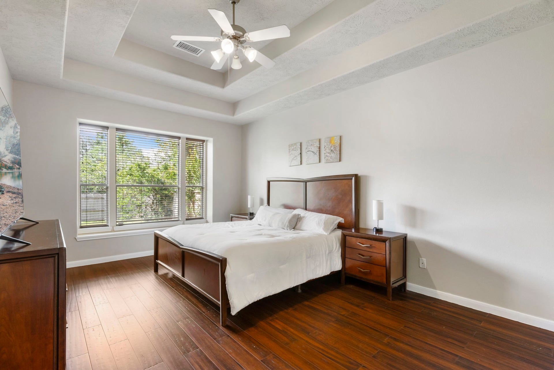 14 N Bardsbrook Circle, The Woodlands, TX 77382 The first-floor primary suite offers a peaceful retreat featuring beautiful wood flooring, a tray ceiling, and large windows overlooking the backyard greenery.