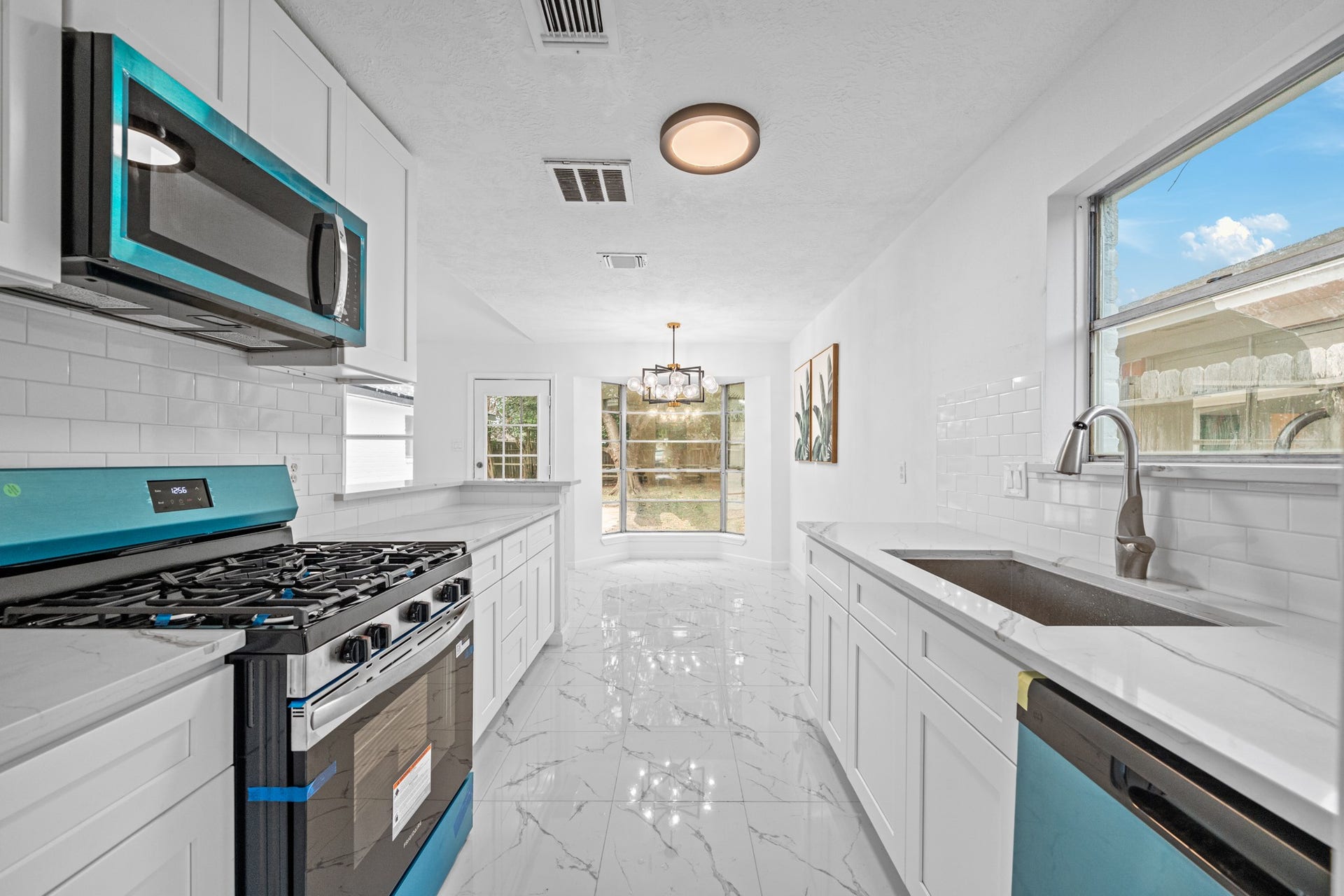 12123 Pompano Lane, Houston, TX 77072 Sleek modern kitchen with stainless steel appliances, white cabinetry, and elegant marble countertops. Ample natural light flows through large windows, highlighting the spacious layout perfect for entertaining.