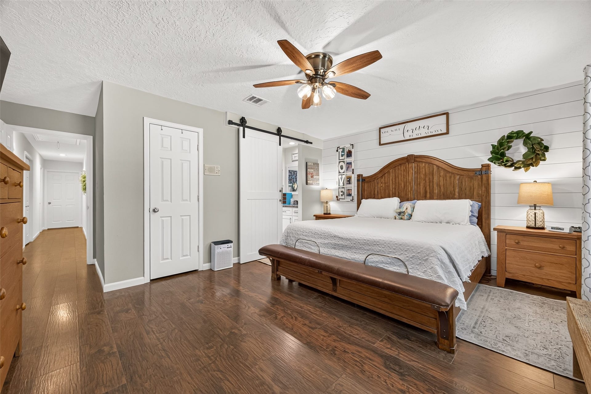 1535 Memorial Drive, Conroe, TX 77304 ANOTHER VIEW OF THE PRIMARY BEDROOM; WE ADDED THE SINGLE CUSTOM BUILT BARN DOOR TO CLOSE WHEN SOMEONE IS IN THE BATHROOM SINK AND VANITY AREA; THE VIEW OF THE HALLWAY LEADING TO THE OTHER SECONDARY BEDROOMS AND GUEST BATHROOM; THE CLOSED DOOR IS THE PRIMARY BEDROOM CLOSET; WE MATCHED THE BARN DOOR WITH ALL HANDLES MATCHING THE REST OF THE CABINETS IN THE HOME