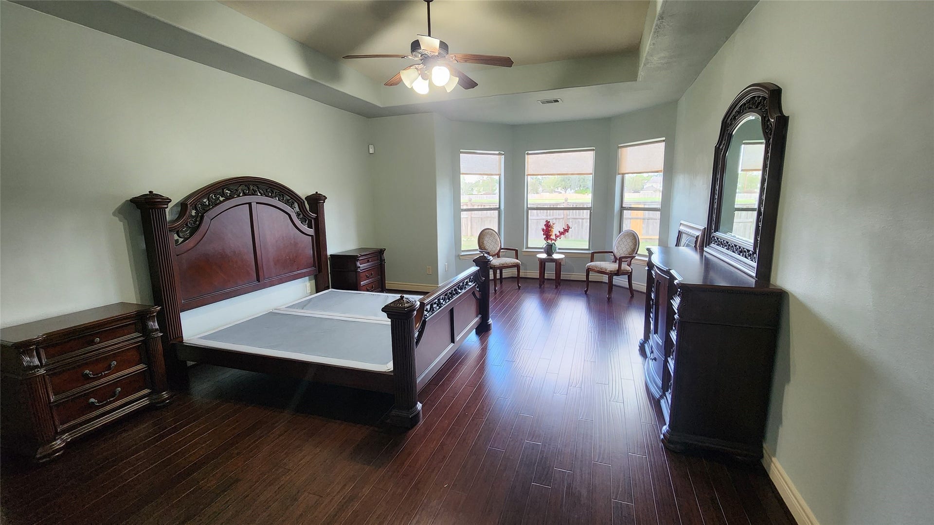 5442 Faircreek Ln Lane, Katy, TX 77450 Luxurious master bedroom featuring elegant dark wood furnishings, expansive windows for abundant natural light, and a stylish tray ceiling that enhances the spacious, serene ambiance.