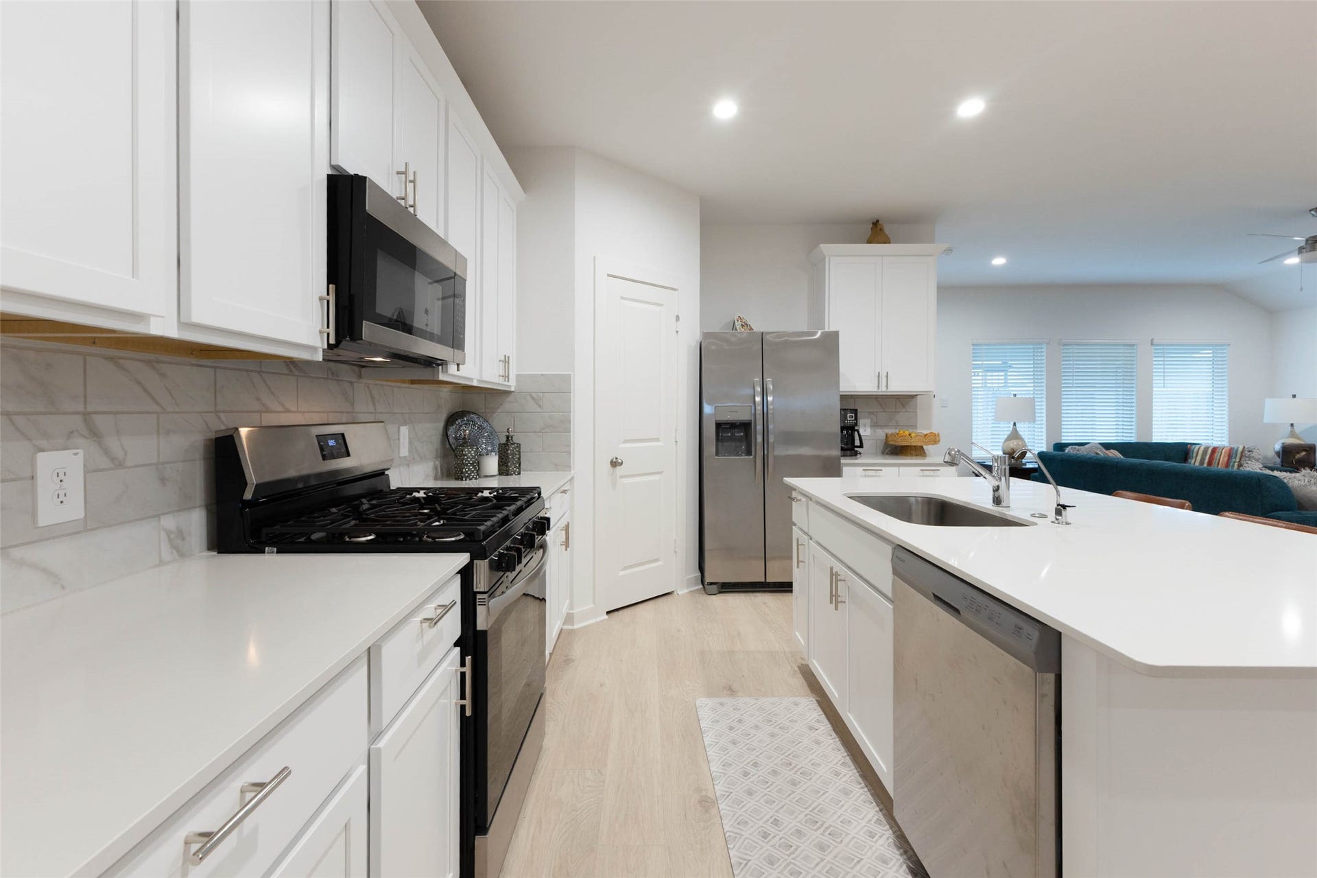 30502 White Cliff Court, Fulshear, TX 77441 Modern kitchen with sleek white cabinetry, stainless steel appliances, and a spacious island featuring a dual sink, seamlessly flowing into the open living area.
