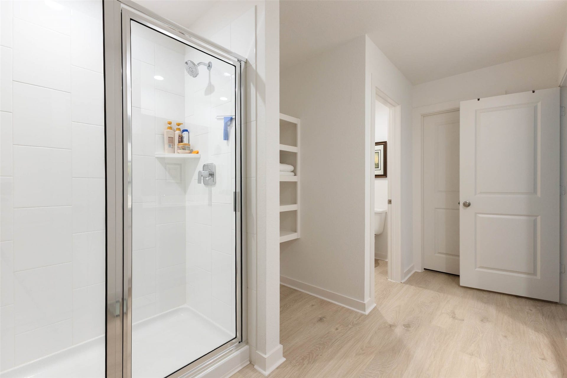 30502 White Cliff Court, Fulshear, TX 77441 Modern bathroom with a sleek glass-enclosed shower, crisp white tiles, and convenient built-in shelving for storage.