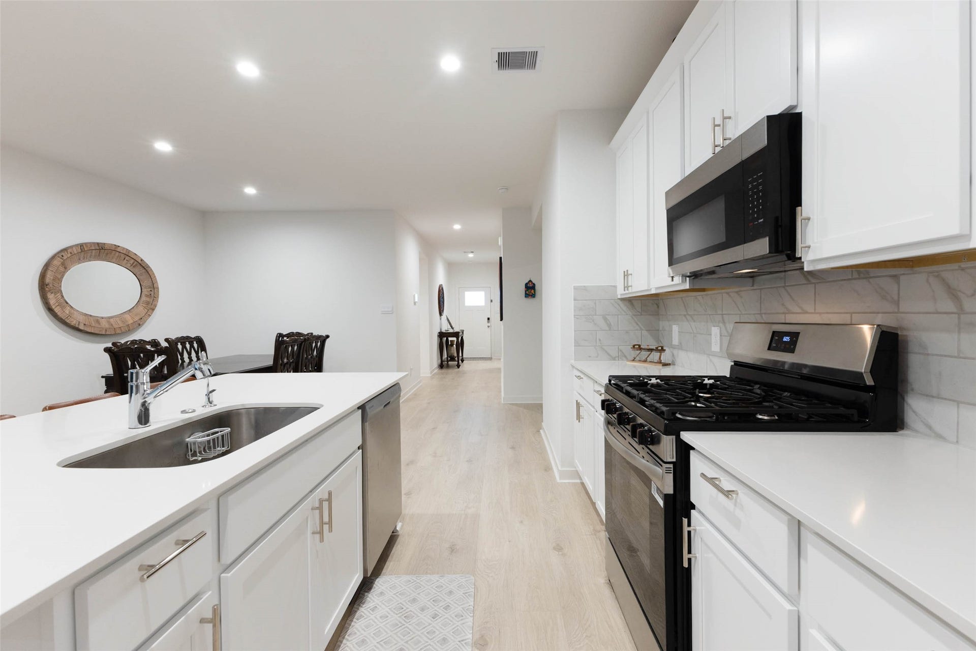 30502 White Cliff Court, Fulshear, TX 77441 Sleek modern kitchen with stainless steel appliances, white cabinetry, and elegant countertops, seamlessly flowing into an open dining area.
