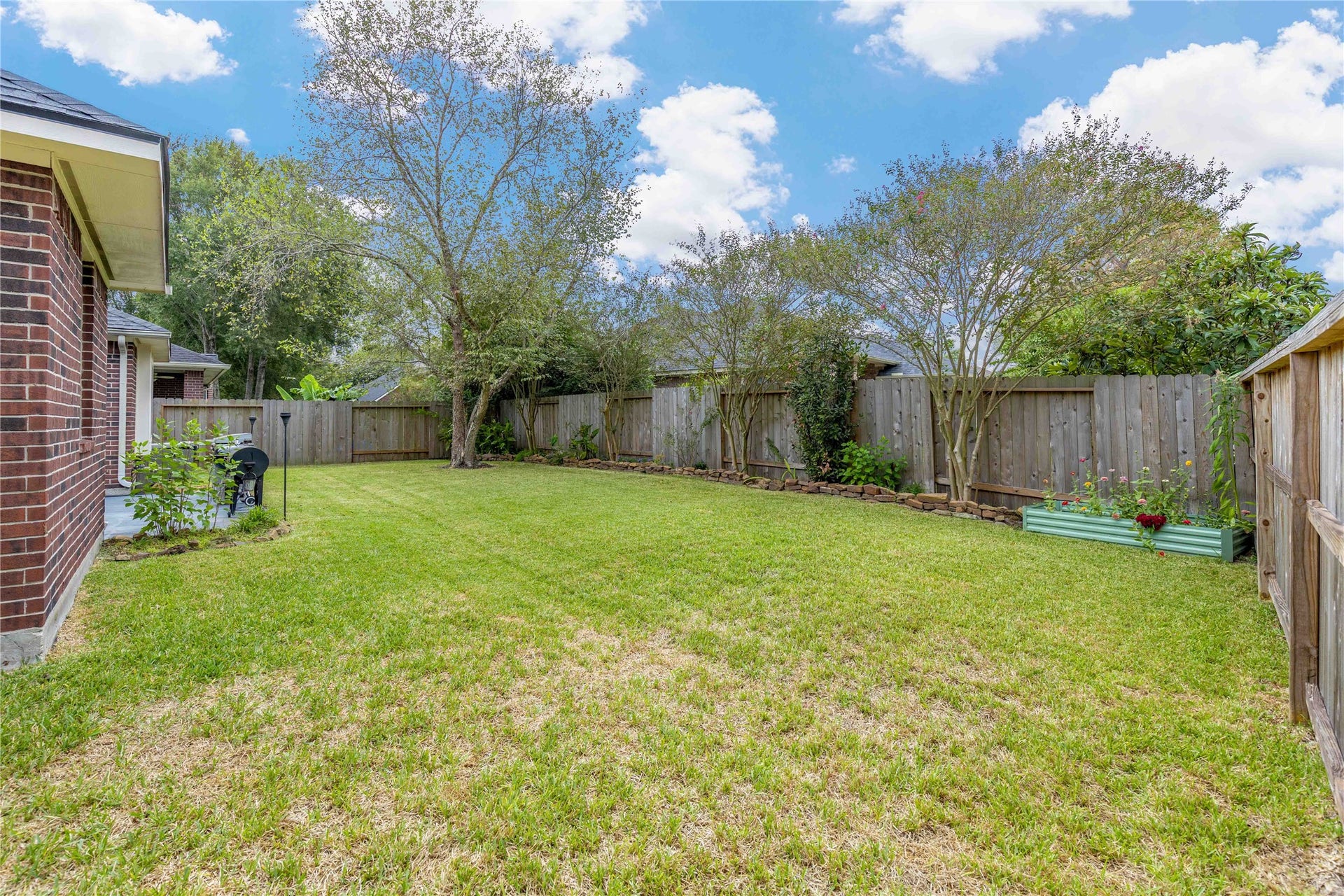 18343 Otter Creek Trail, Humble, TX 77346 Charming backyard with lush green lawn, mature trees, and a wooden fence providing privacy. Perfect for outdoor gatherings and relaxation.