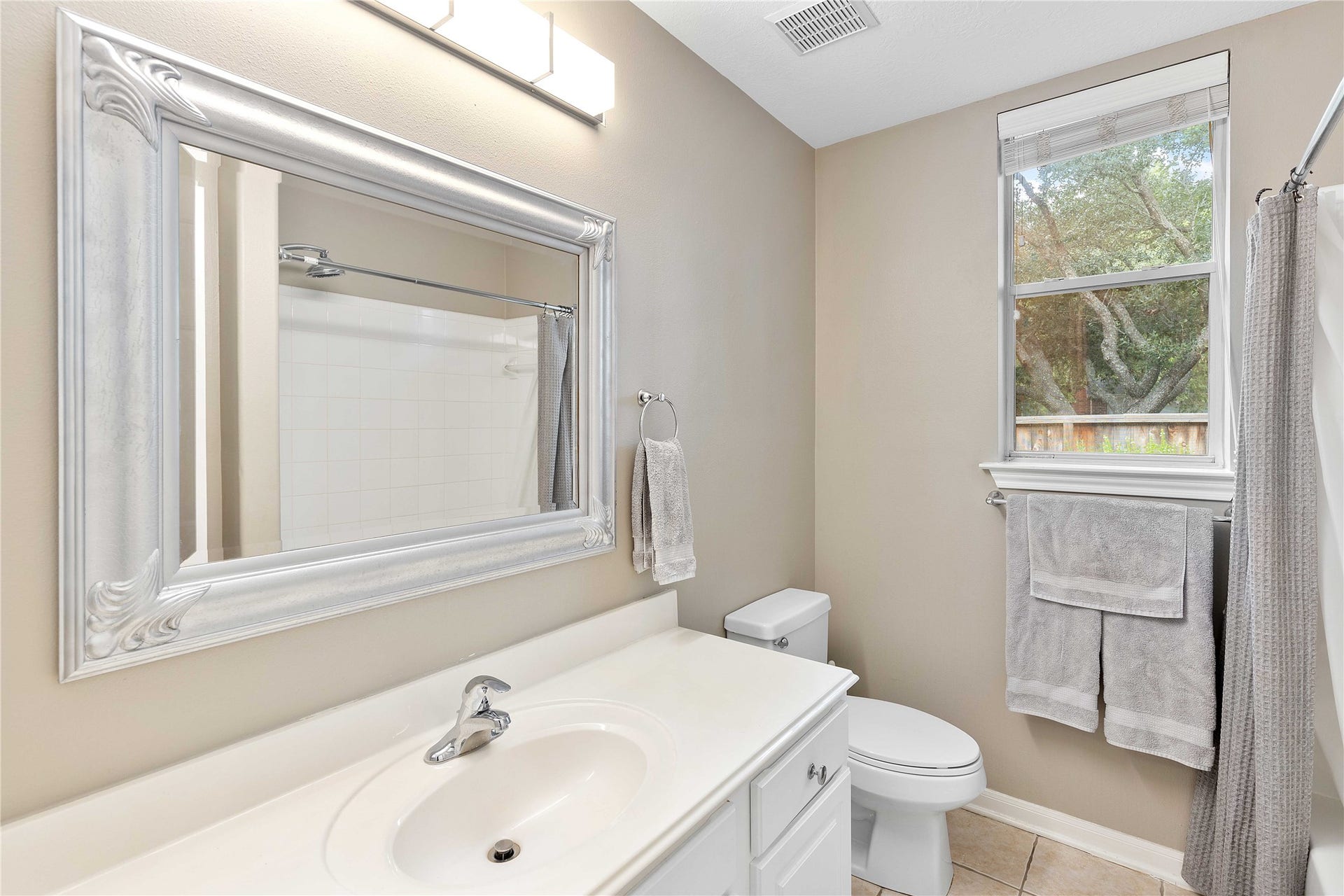 18343 Otter Creek Trail, Humble, TX 77346 Bright and inviting bathroom featuring a sleek vanity with a large framed mirror, modern fixtures, and a window providing natural light.