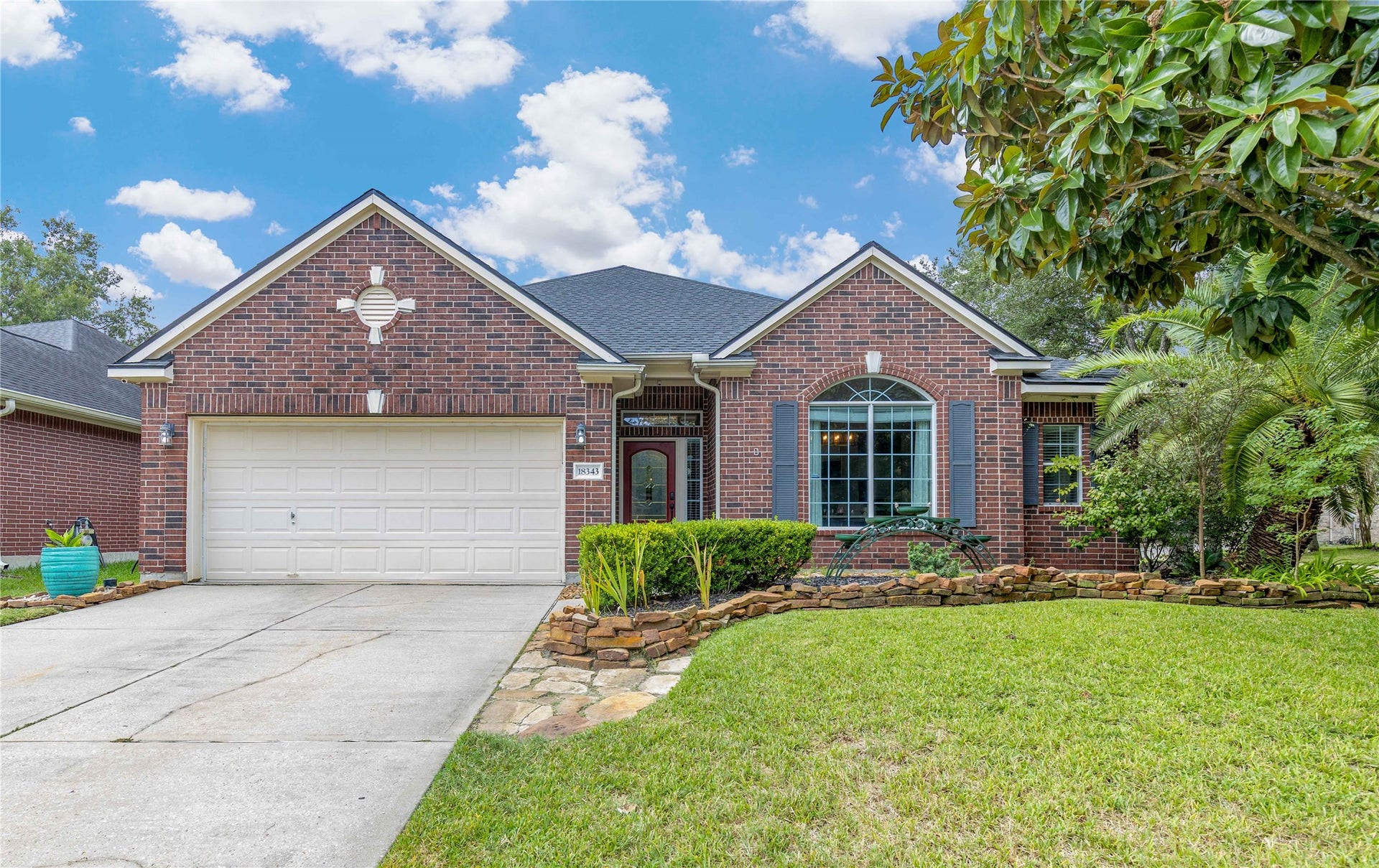 18343 Otter Creek Trail, Humble, TX 77346 Charming brick home with a welcoming arched window and manicured landscaping, featuring a spacious two-car garage and inviting front walkway.