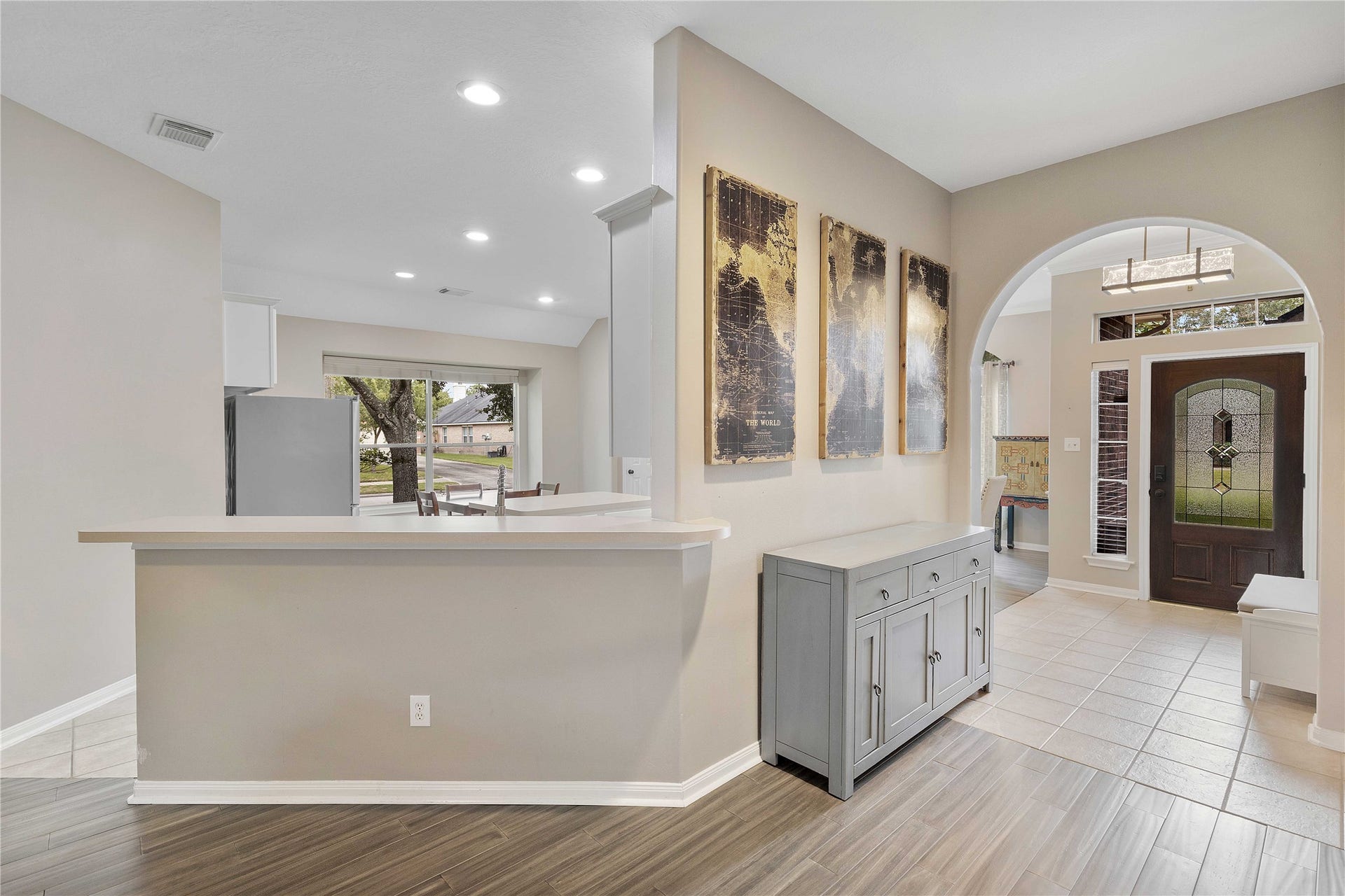 18343 Otter Creek Trail, Humble, TX 77346 Inviting entryway with elegant flooring, an arched doorway, and a tasteful accent wall. A contemporary kitchen bar opens up to a spacious living area, enhanced by natural light from large windows.