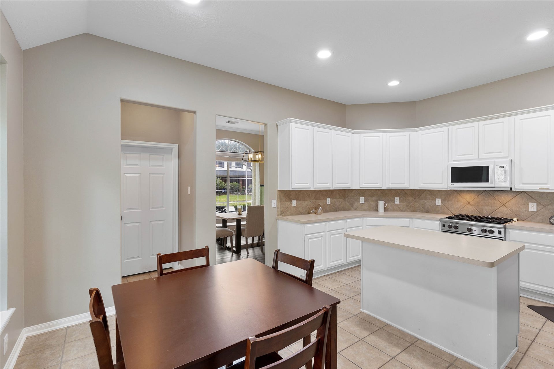 18343 Otter Creek Trail, Humble, TX 77346 Bright and spacious kitchen with modern white cabinetry, a central island, and tile flooring, seamlessly connected to a dining area with yard views.