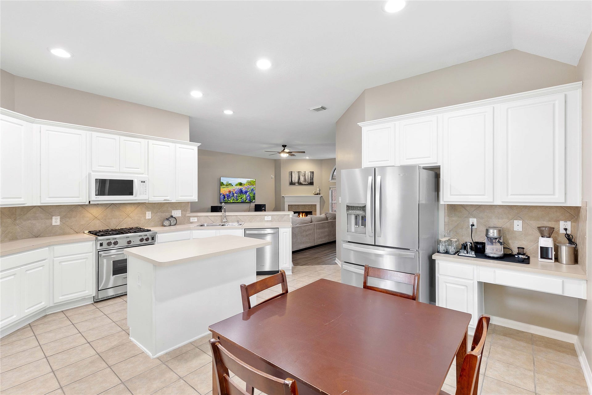18343 Otter Creek Trail, Humble, TX 77346 Spacious kitchen with modern stainless steel appliances, ample white cabinetry, and a central island, flowing seamlessly into an inviting living area with cozy seating and a fireplace.