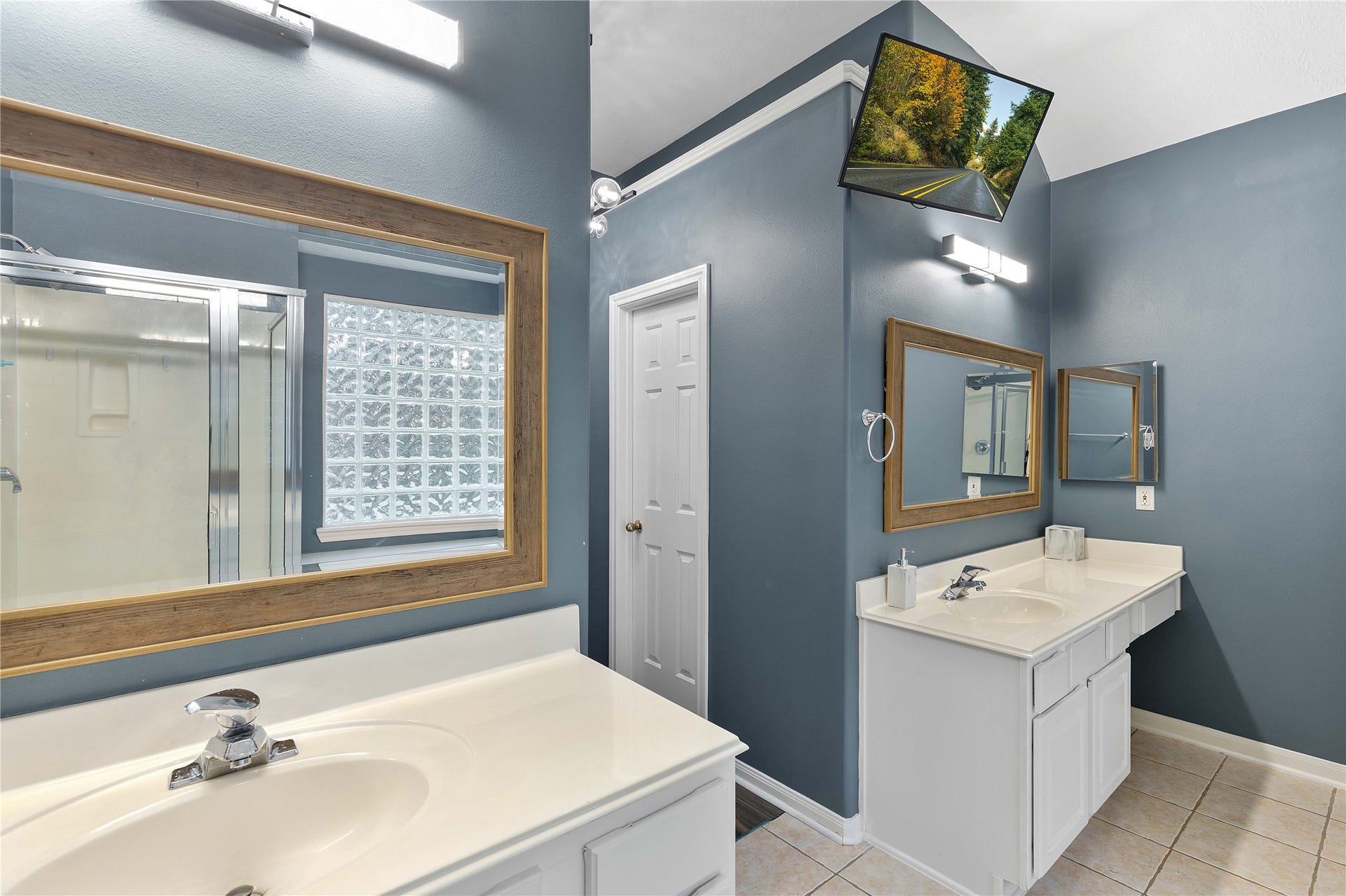 18343 Otter Creek Trail, Humble, TX 77346 Bright and spacious bathroom featuring dual sinks with modern fixtures, elegant framed mirrors, and a stylish glass block window for natural light.