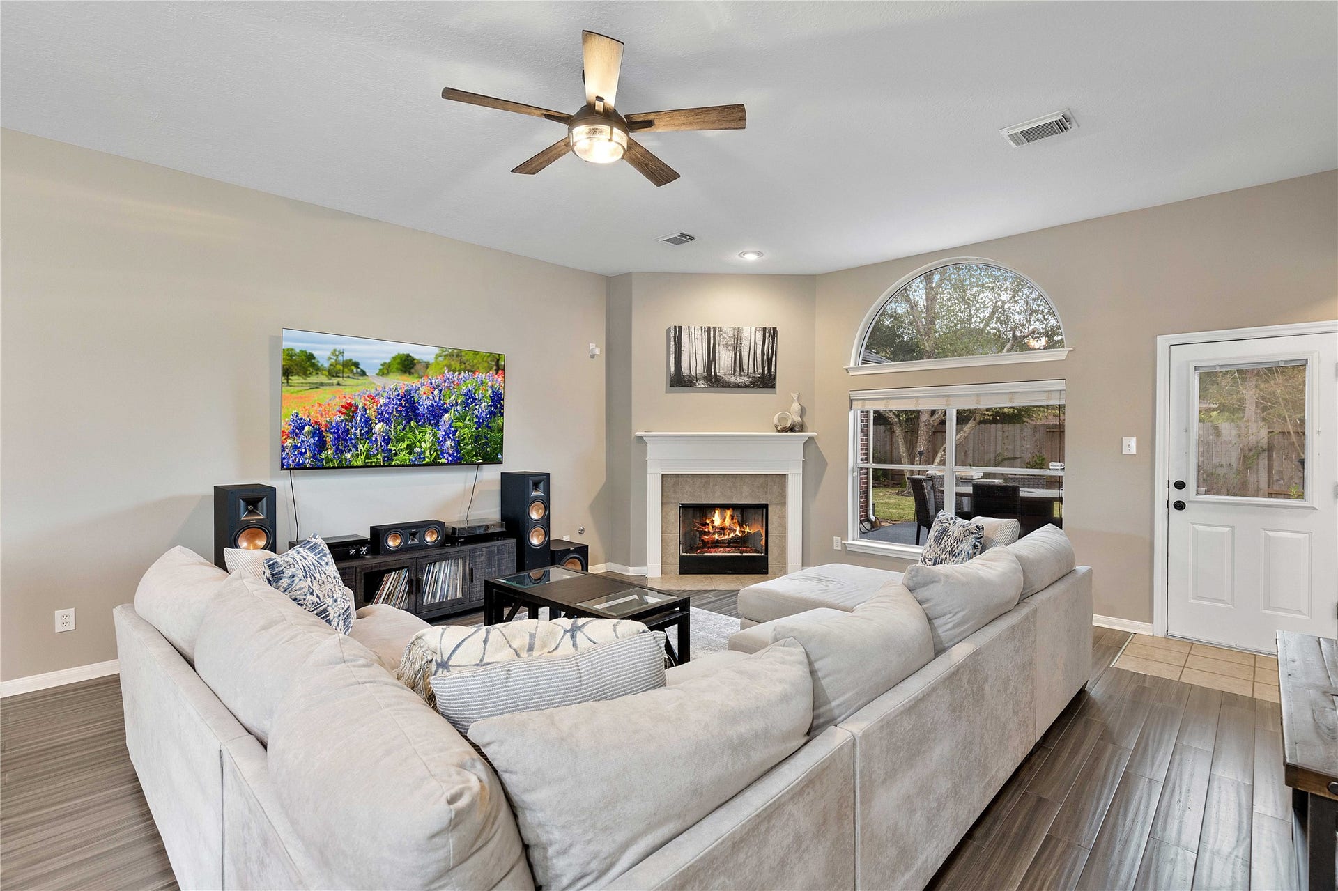 18343 Otter Creek Trail, Humble, TX 77346 Spacious living room with a cozy fireplace, sleek flooring, and abundant natural light streaming through large windows.