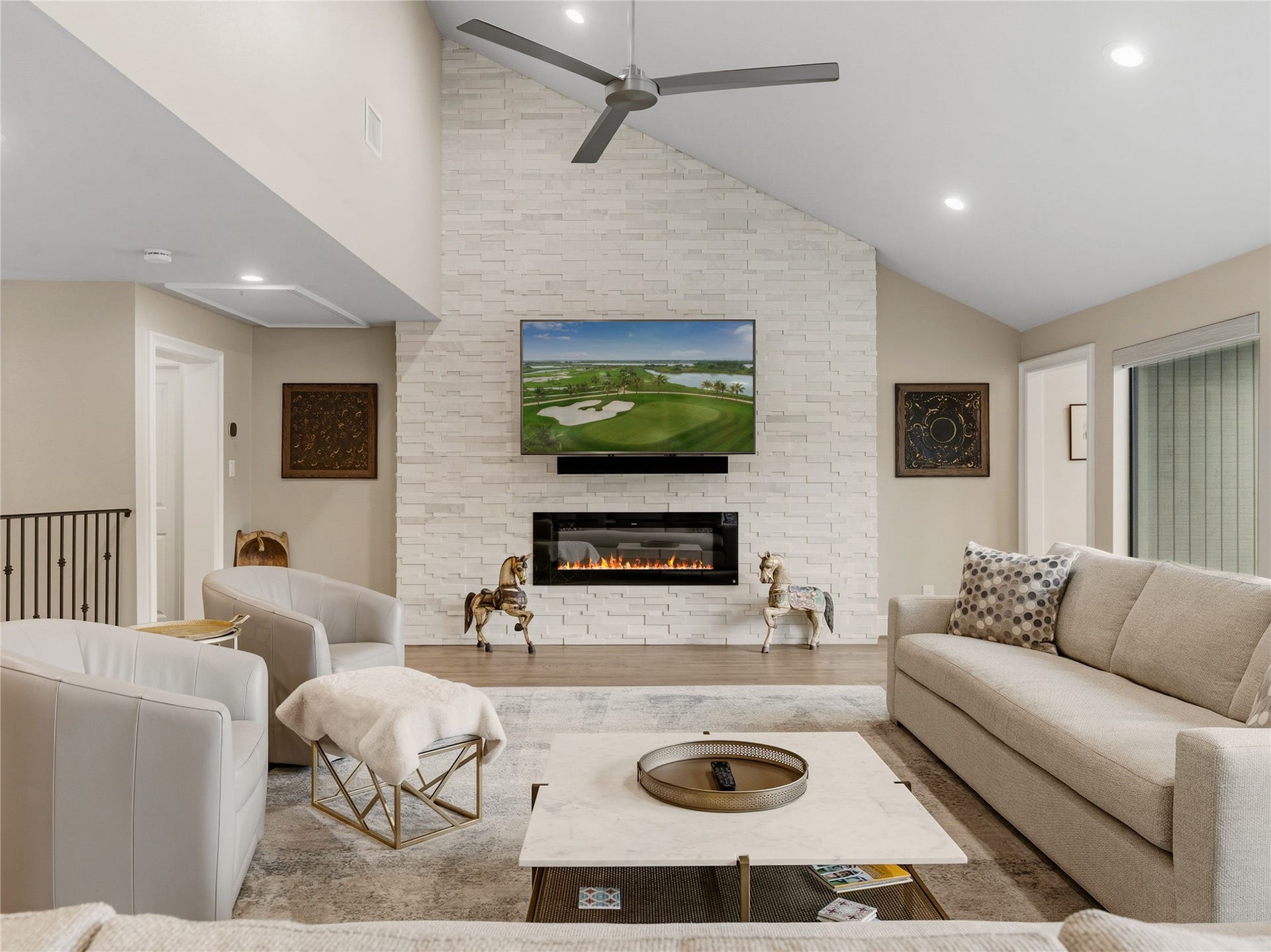 75 Huntsmans Horn Circle, The Woodlands, TX 77380 Elegant living room featuring a vaulted ceiling, modern fireplace, and sleek ceiling fan. Cozy seating areas and a large TV enhance relaxation and entertainment.