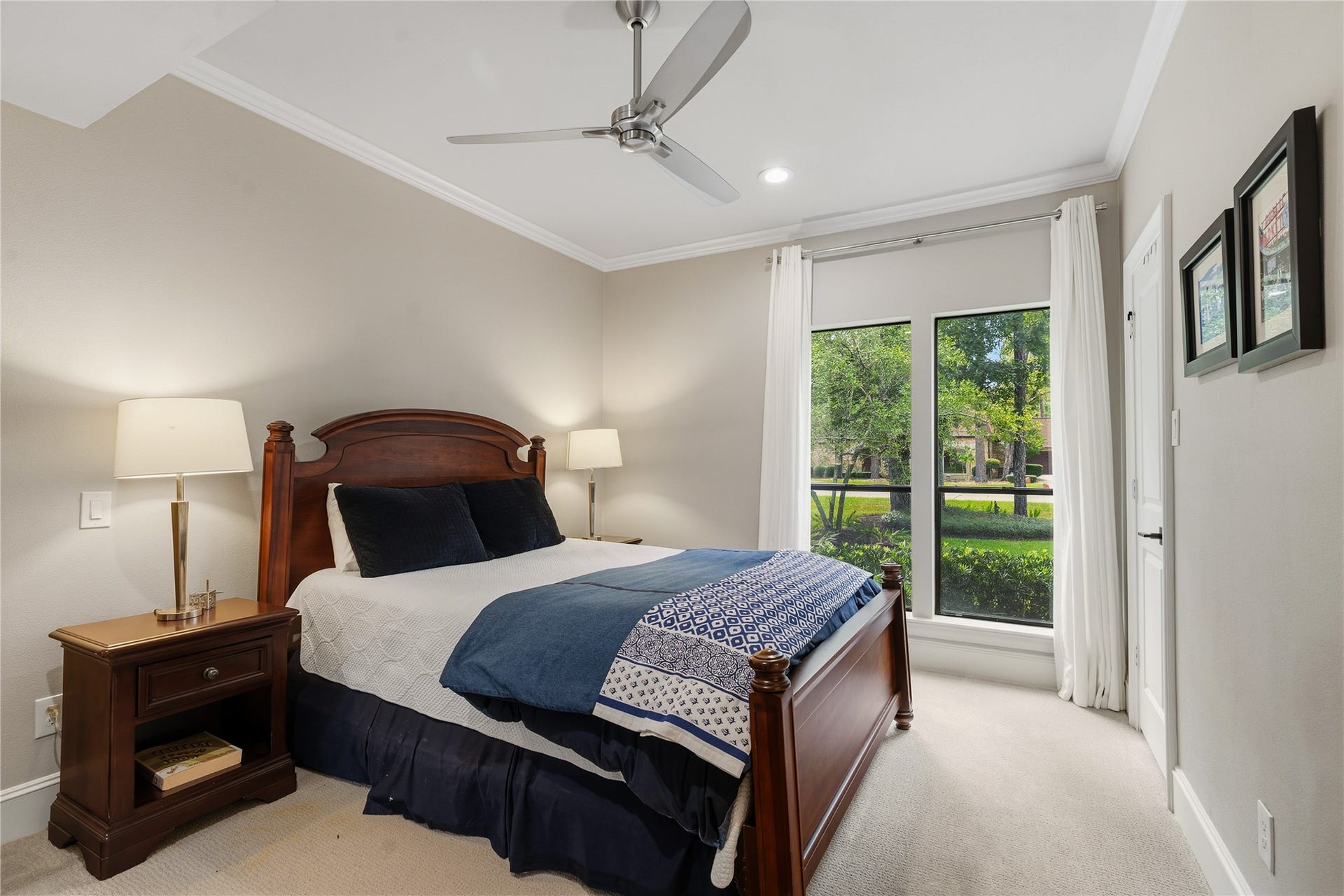 75 Huntsmans Horn Circle, The Woodlands, TX 77380 Charming bedroom with a cozy wooden bed frame, elegant bedside lamps, and large windows offering a serene view of the lush greenery outside.