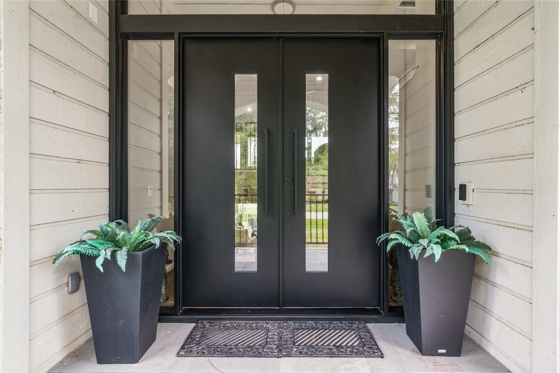 75 Huntsmans Horn Circle, The Woodlands, TX 77380 Modern double doors with sleek black finish and vertical glass panels, flanked by tall planters with lush greenery, create an inviting entrance.