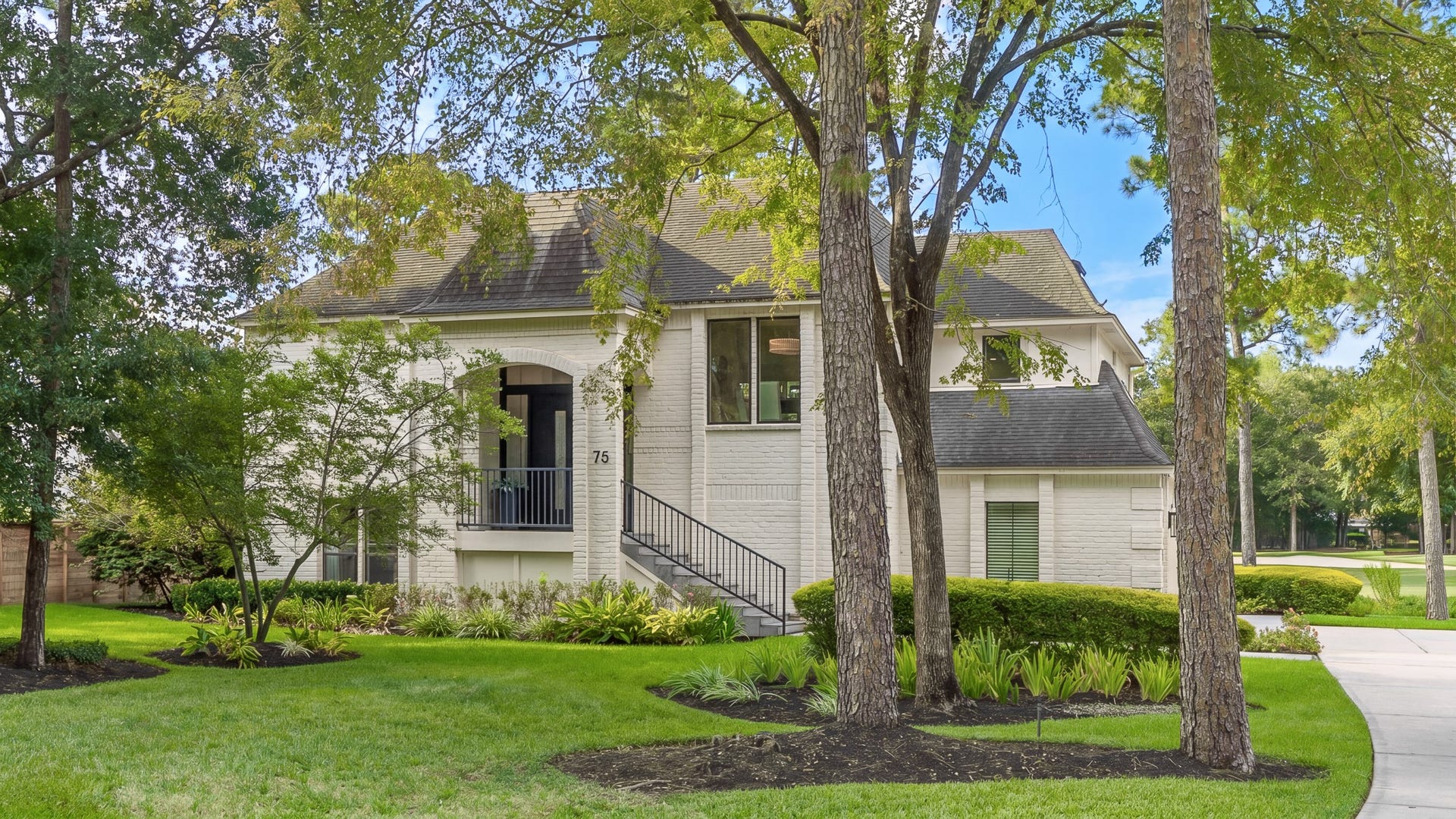 75 Huntsmans Horn Circle, The Woodlands, TX 77380 Charming home nestled among mature trees, featuring a classic brick exterior and a welcoming front porch, all set on a beautifully landscaped lawn.