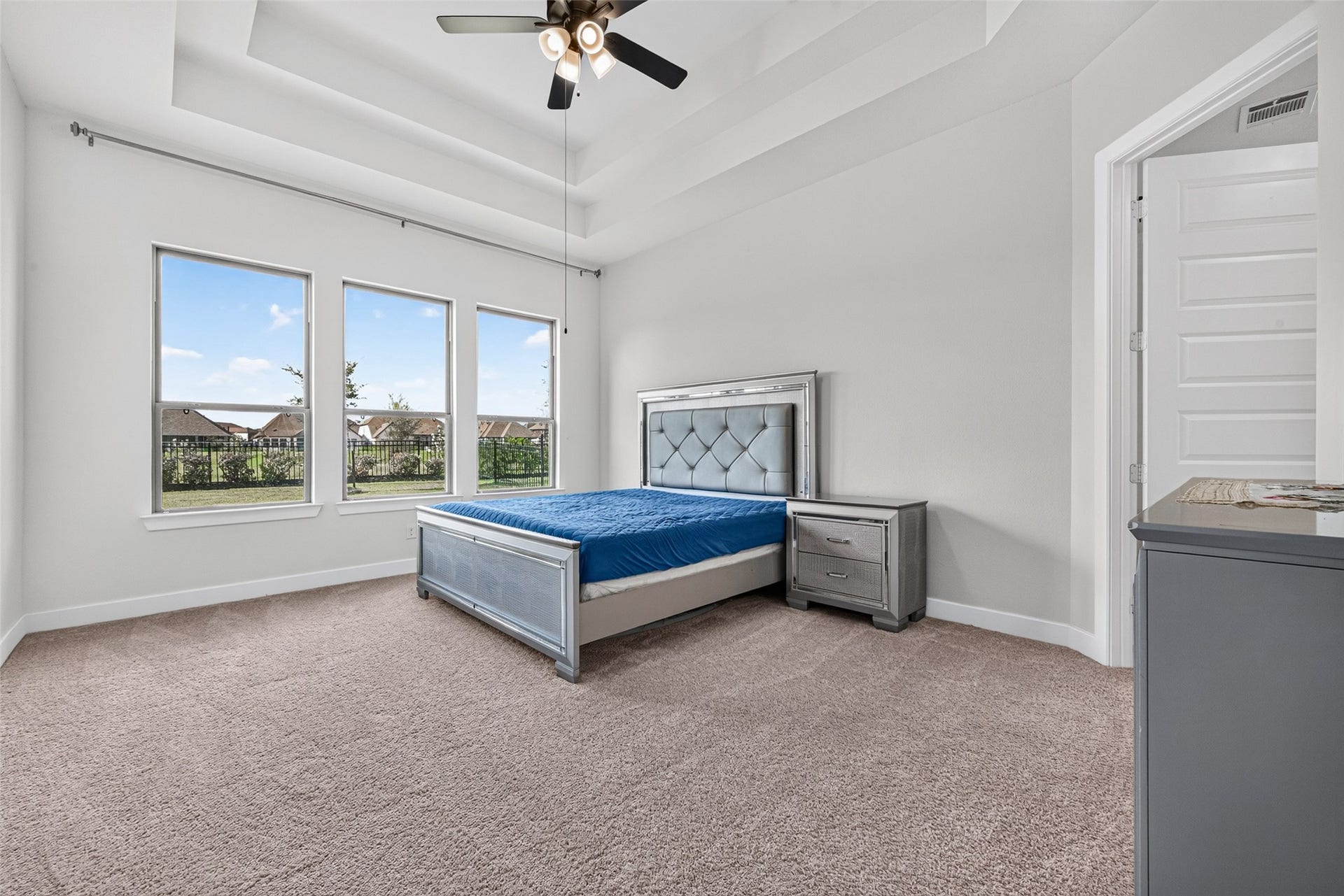 2511 Falling Fig Lane, Richmond, TX 77406 A luxurious primary bedroom featuring elegant tray ceilings and a stunning wall of windows, creating a spacious, sophisticated retreat filled with natural light and timeless appeal.