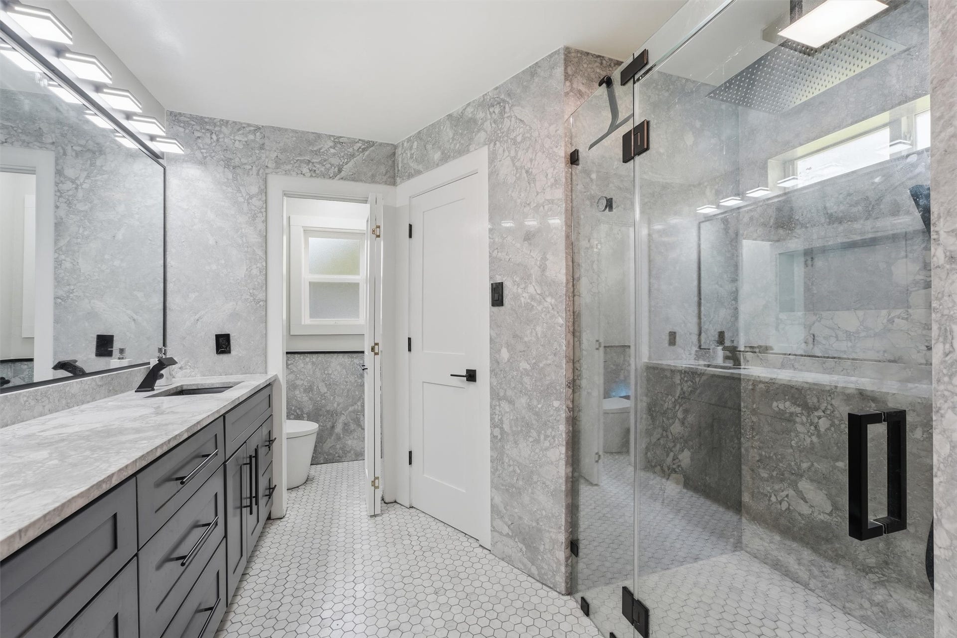 1718 Laurel Springs Lane, Kingwood, TX 77339 The main primary bathroom features a large glass-enclosed walk-in shower with natural quartzite walls, a double vanity with black fixtures, distinctive hexagonal tile flooring, and closets on either side of the shower.