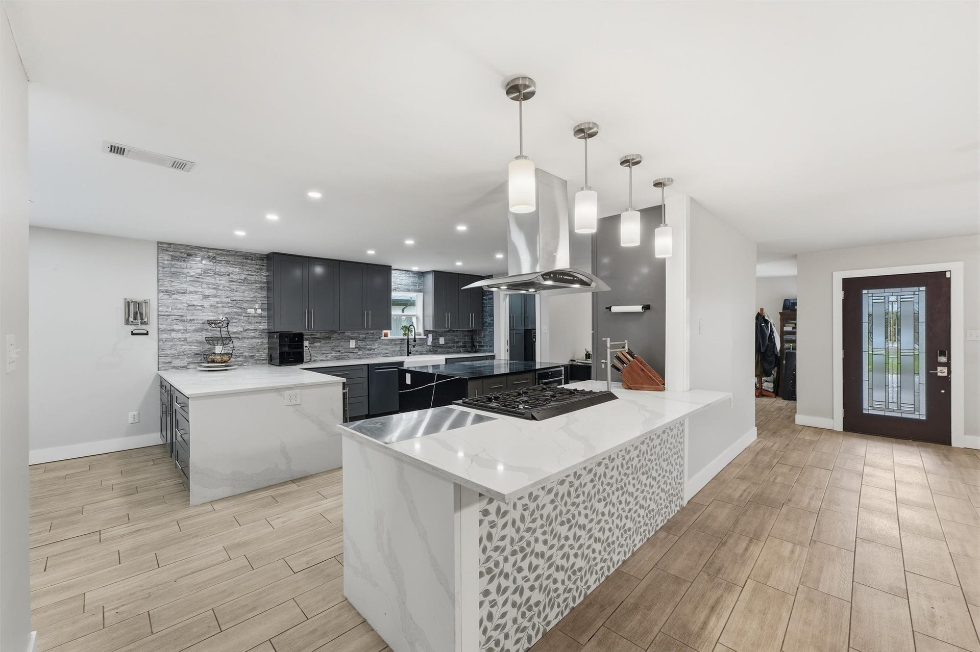 1718 Laurel Springs Lane, Kingwood, TX 77339 The kitchen offers extensive counterspace, dark cabinetry, a gas cooktop with a convenient pot filler, stainless steel range hood, pendant lighting, and decorative tile accents.