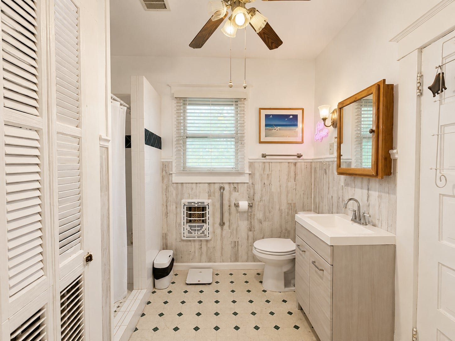 Alternate view highlights the vanity, tiled shower, window, and spacious layout. A ceiling fan and ample built-in storage add functionality to the space.