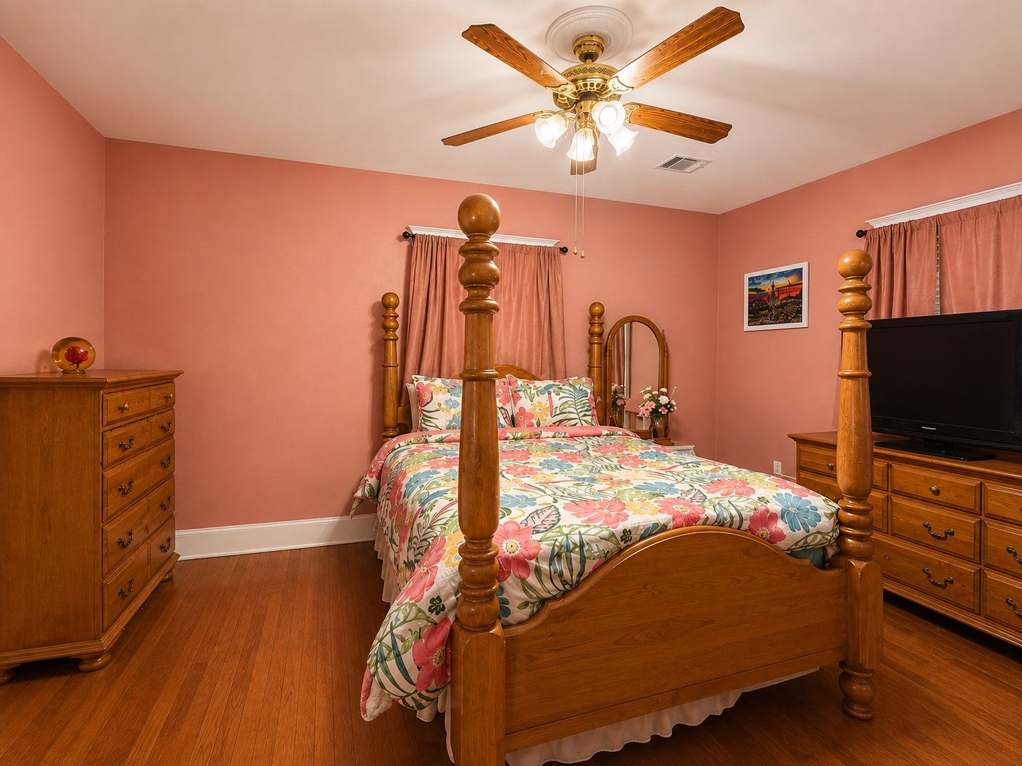 A second view showcases the bedrooms generous proportions, wood flooring, multiple windows, and ceiling fan, with plenty of wall space for additional furniture.