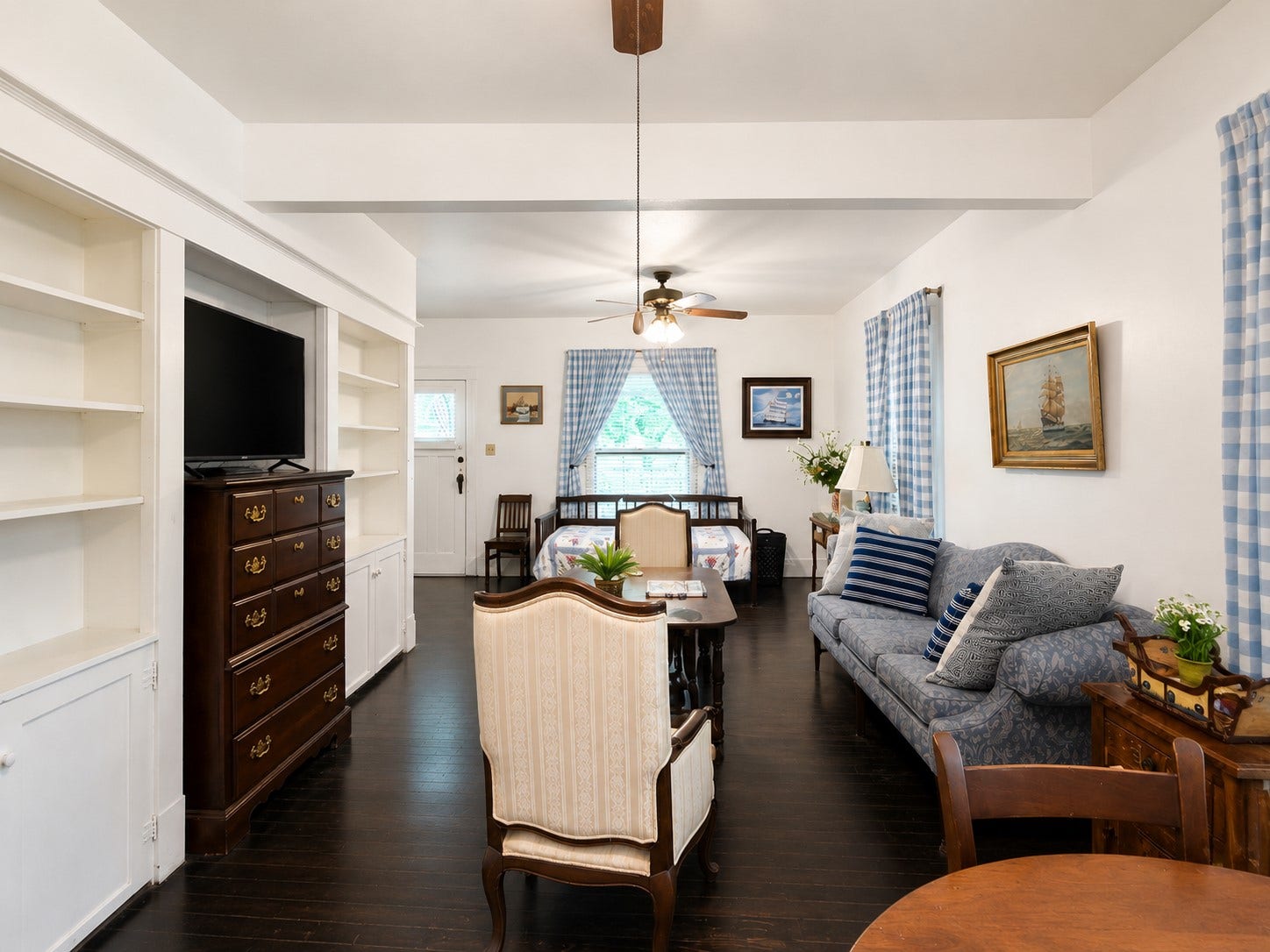 Wide-angle view showcases the spacious living area with built-in shelving and cabinetry, dark wood flooring, ceiling fans, and abundant natural light. The extended layout provides flexibility for multiple seating and gathering areas.