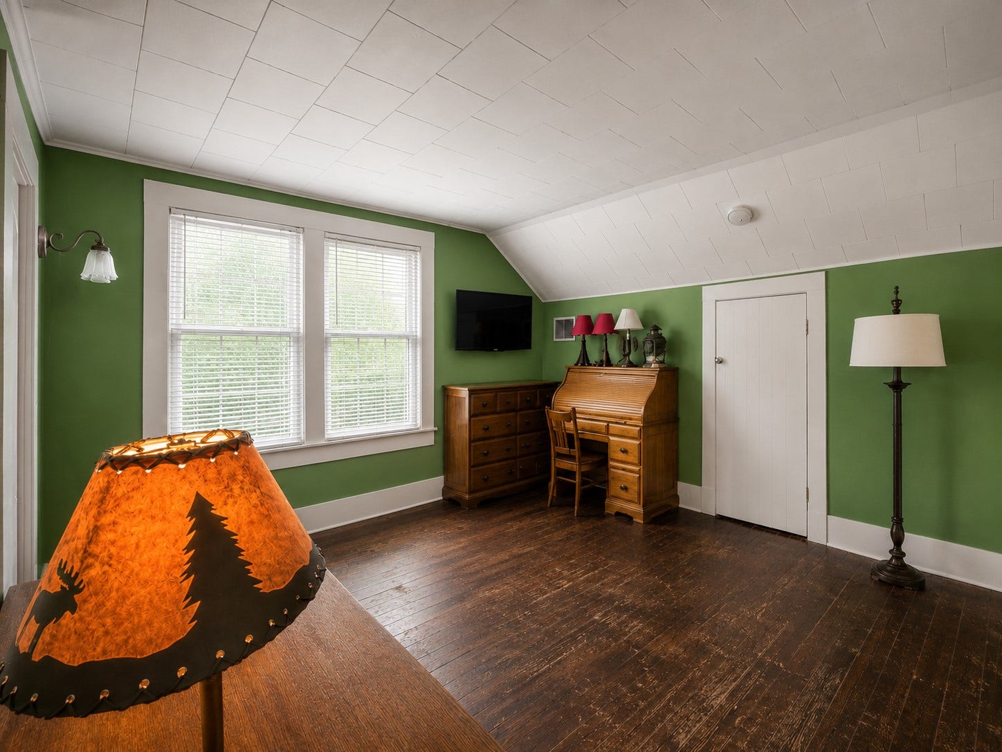 This angle showcases the rooms distinctive sloped ceiling, generous floor space, and large double window. Wood flooring and traditional trim continue the homes character, with ample room for a desk or additional furnishings.