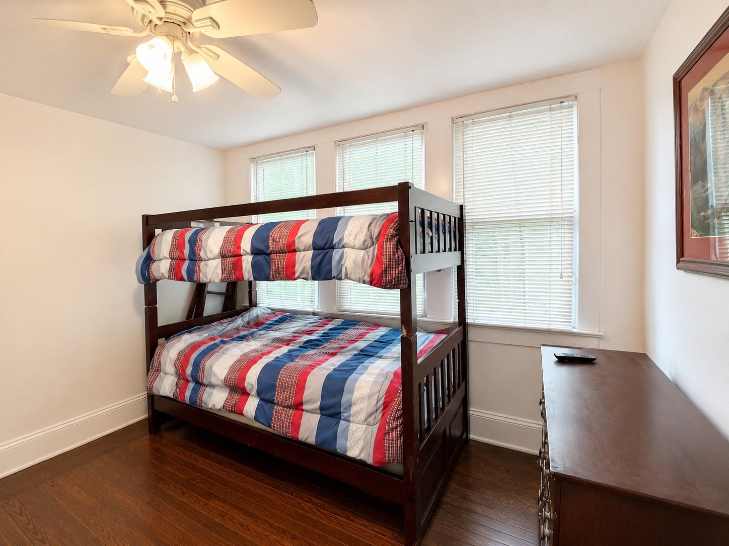 Bright loft area features warm wood flooring, a ceiling fan, and a wall of windows that brings in abundant natural light. Neutral walls and classic white trim create a clean, versatile backdrop.