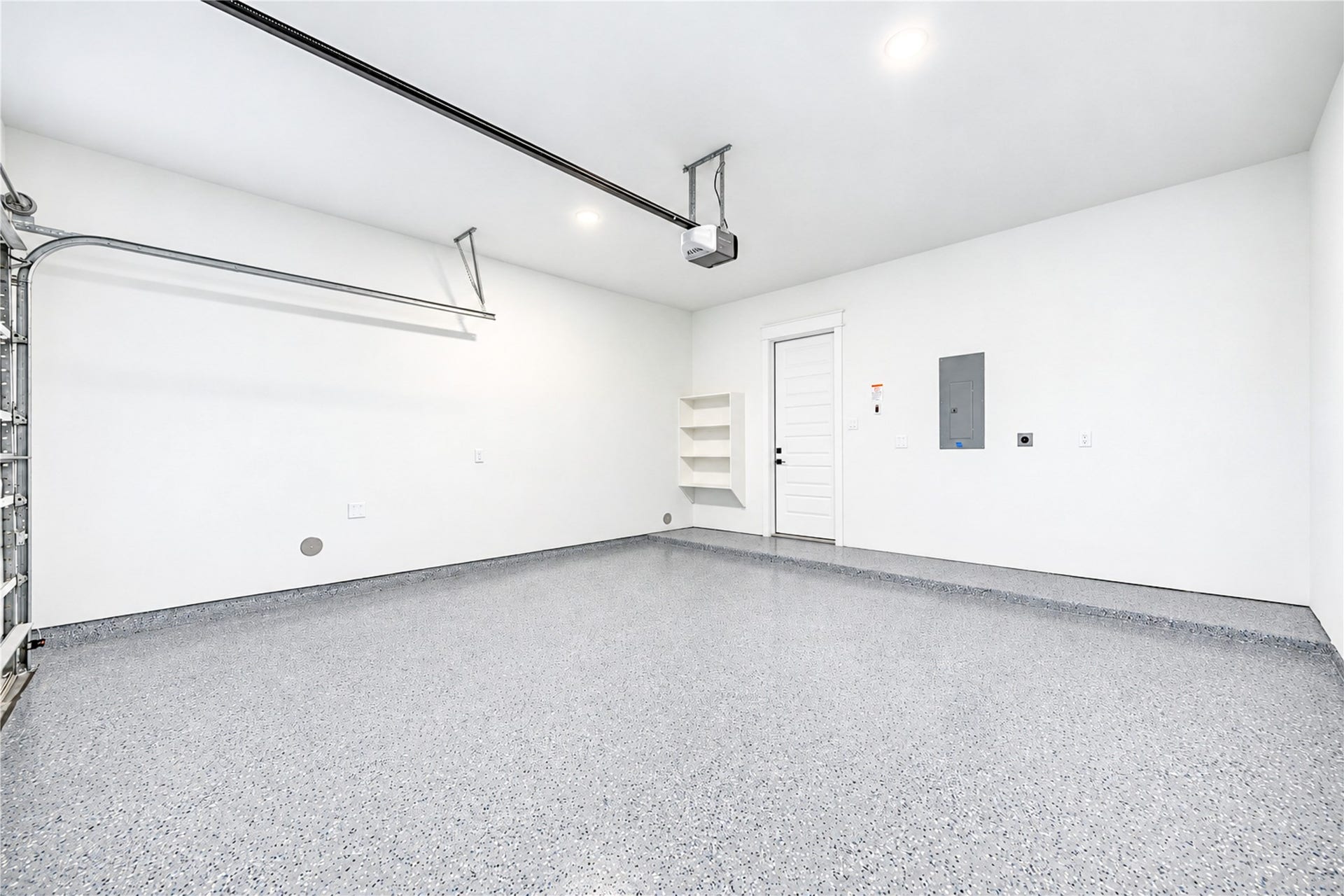Pristine garage space featuring a durable grey epoxy floor coating, custom built-in shelving, bright recessed lighting, and direct interior access.
