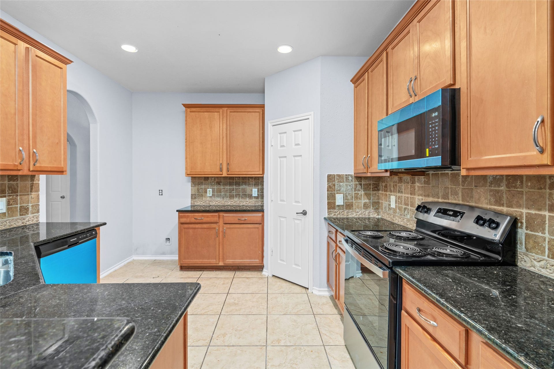 24519 Evangeline Springs Lane, Katy, TX 77494 Functional kitchen with wood cabinetry, black granite countertops, tiled flooring, and built-in appliances. The arrangement offers substantial cabinet storage and counter space for everyday cooking and meal preparation.