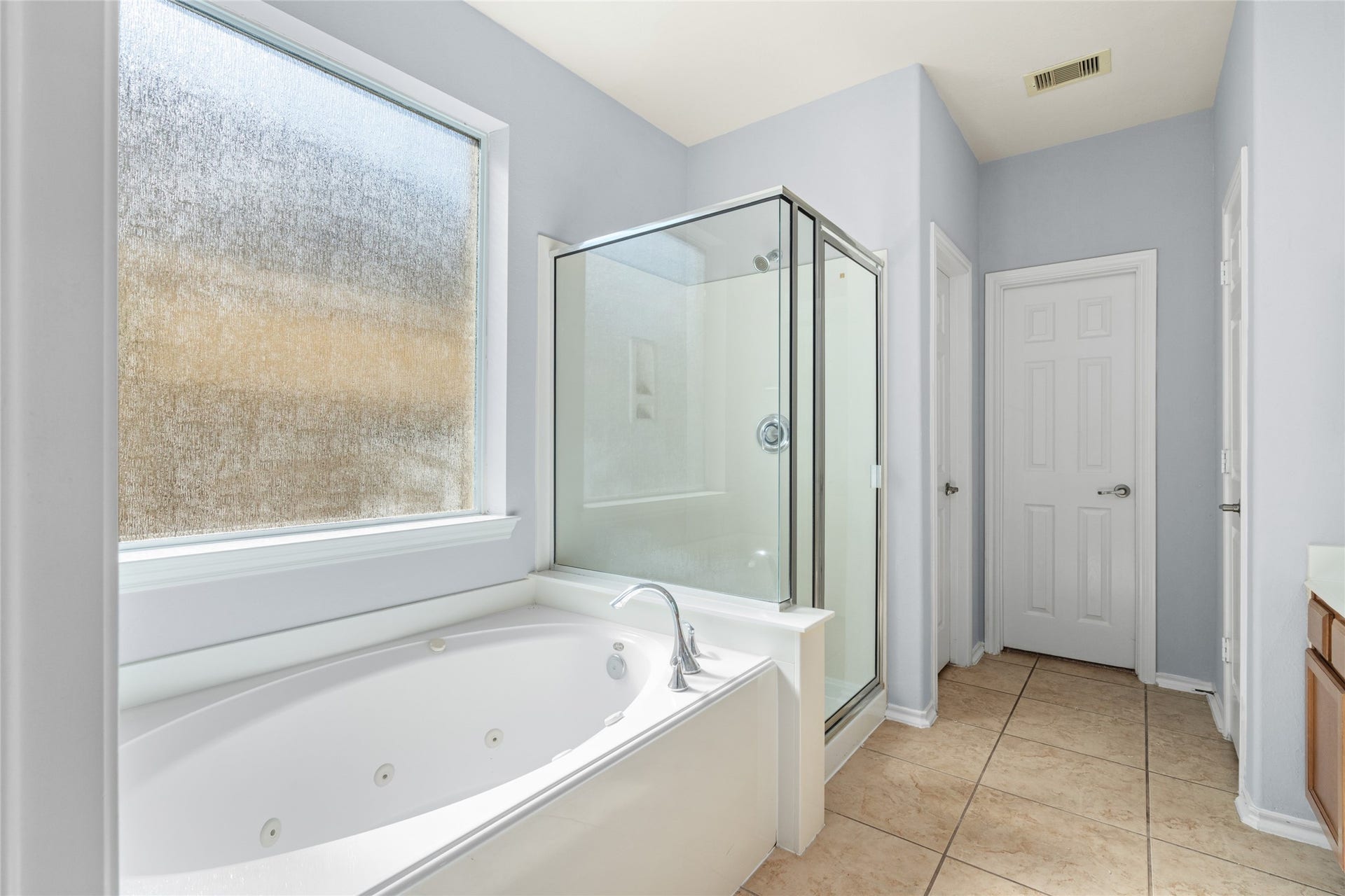 24519 Evangeline Springs Lane, Katy, TX 77494 Primary bathroom featuring a corner jetted tub, separate glass-enclosed shower, and natural light from a large window. The separate bathing options provide flexibility for a quick morning routine or a more relaxing end-of-day soak.