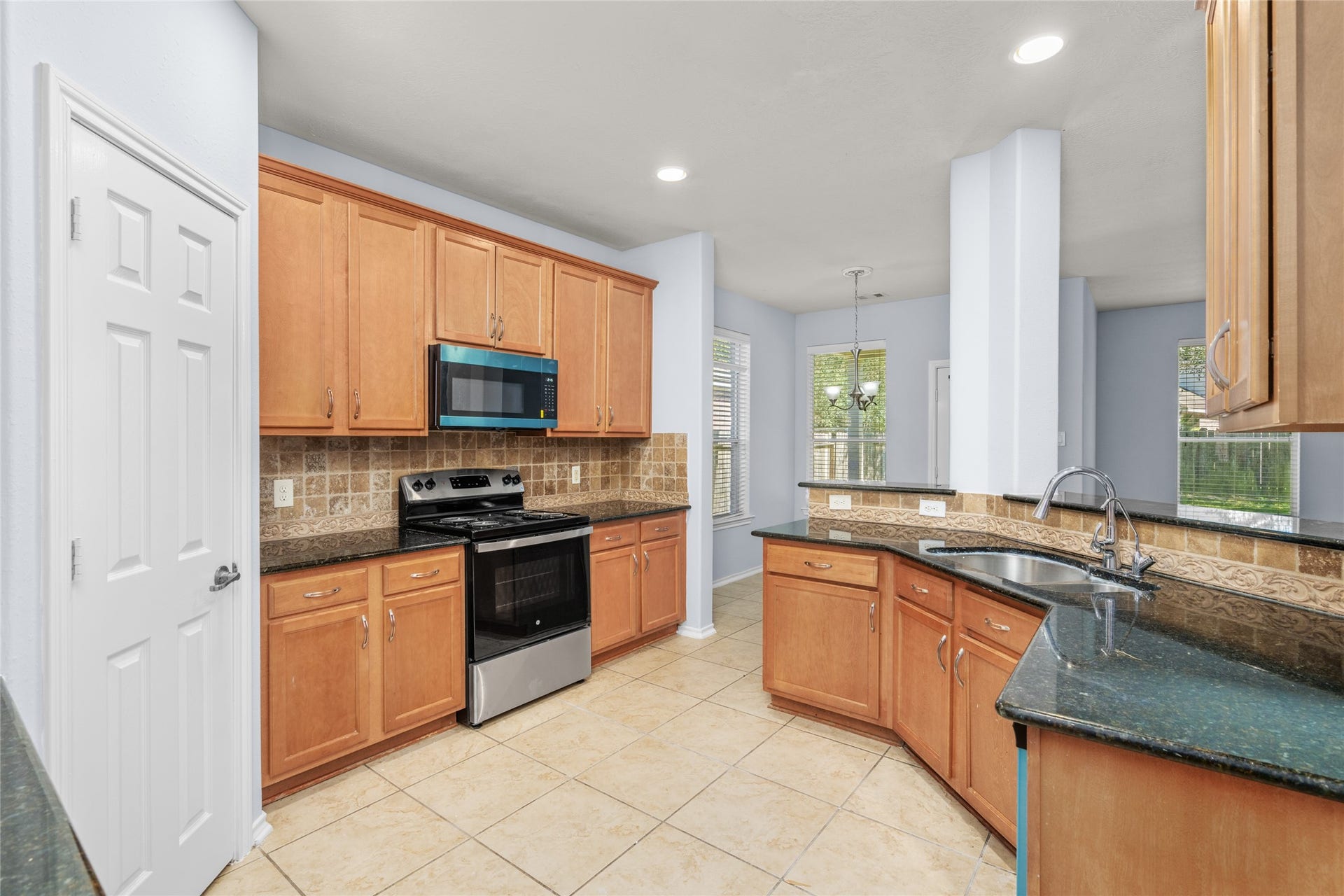 24519 Evangeline Springs Lane, Katy, TX 77494 Alternate kitchen view highlighting the cabinetry, black granite work surfaces, built-in microwave, electric range, and tiled flooring. The combination of storage and accessible counter space supports an efficient everyday cooking routine.