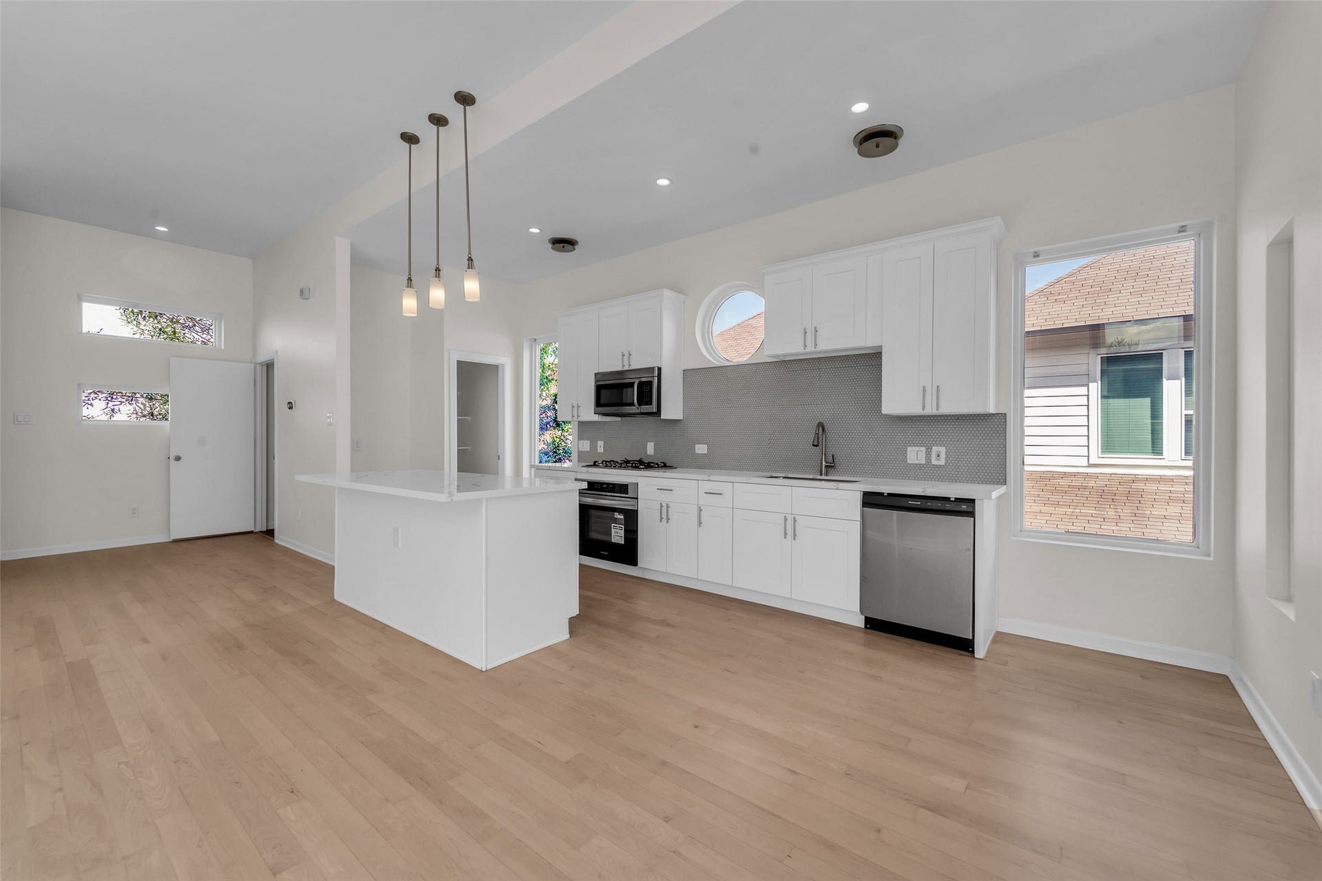 Bright and airy kitchen with modern white cabinetry, sleek stainless steel appliances, and a spacious island with pendant lighting, complemented by natural wood floors and ample windows for natural light.