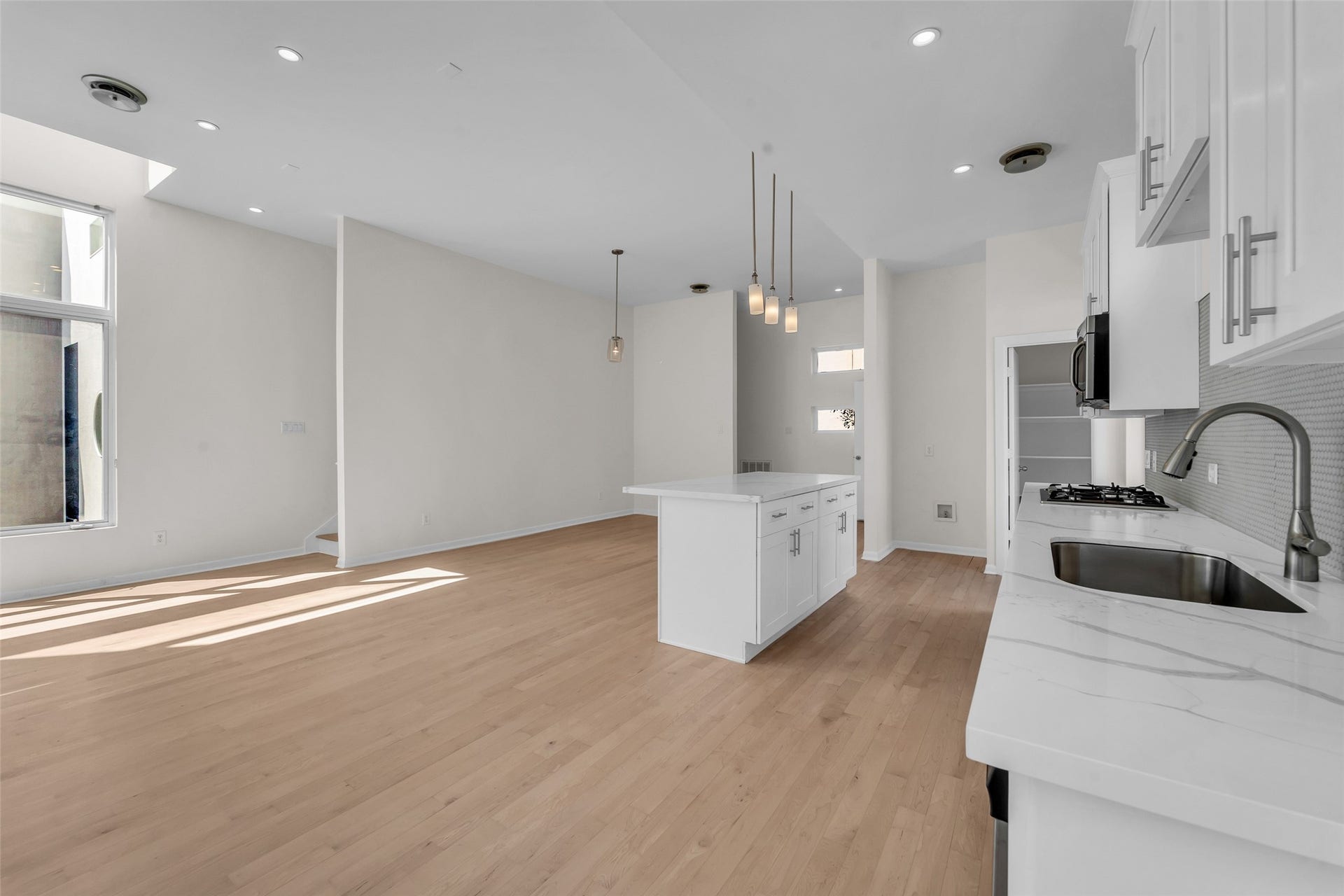 Bright and modern open-concept kitchen and living area featuring sleek white cabinetry, a central island, and ample natural light from large windows.