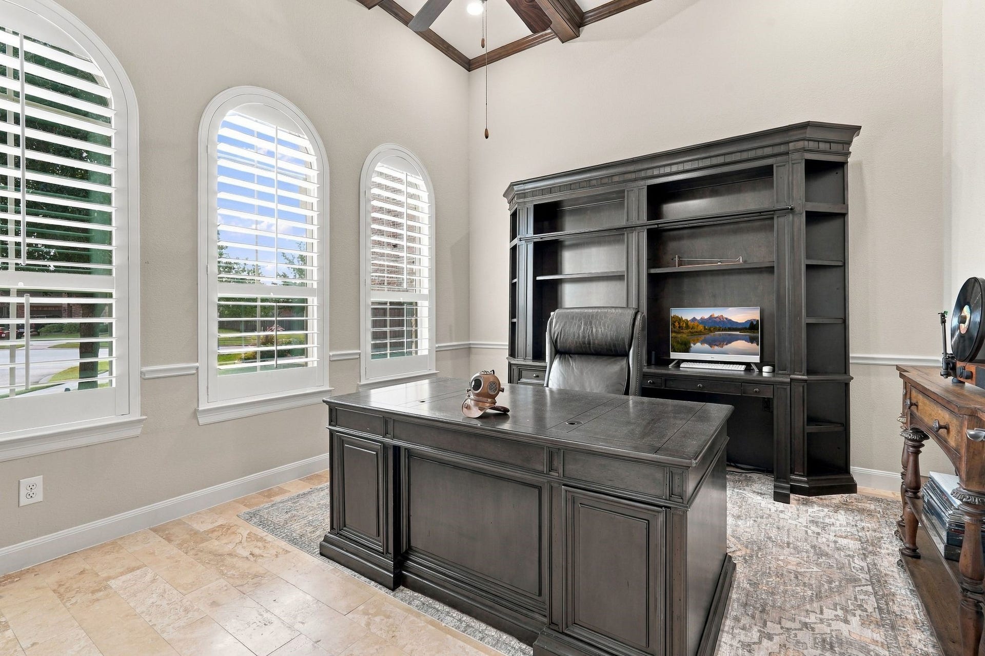 13714 Arcott Bend Drive, Tomball, TX 77377 Elegant private home office featuring soaring ceilings with decorative wood beams, three beautiful arched windows with plantation shutters, and natural stone flooring. Abundant natural light creates an inviting and functional workspace, ideal for working from home.