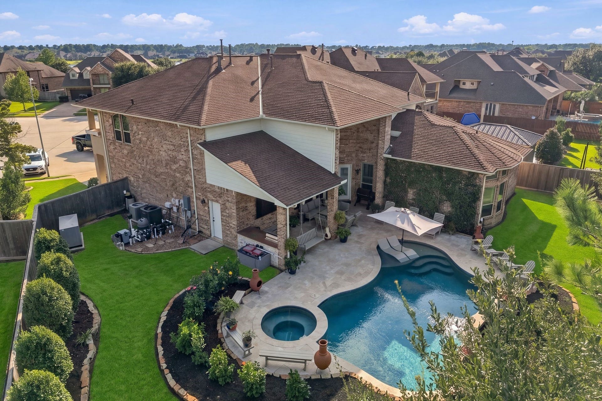 13714 Arcott Bend Drive, Tomball, TX 77377 Stunning aerial view of the resort-style backyard showcasing a custom-designed pool and spa, expansive travertine decking, covered outdoor living area with kitchen, and beautifully manicured landscaping. Generous green space and mature trees provide the perfect balance of luxury outdoor entertaining and everyday relaxation.