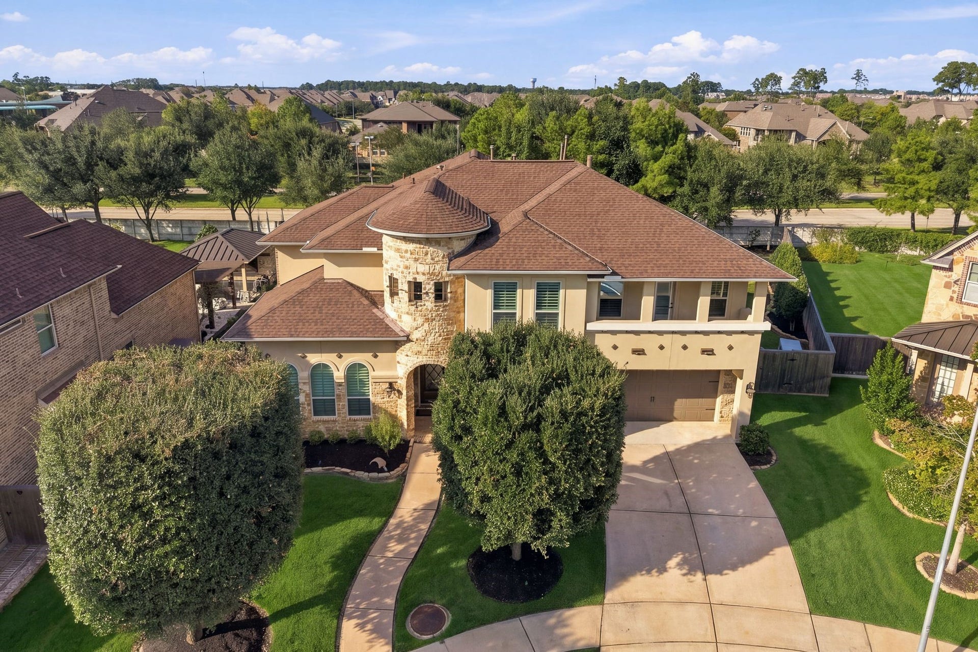 13714 Arcott Bend Drive, Tomball, TX 77377 Impressive aerial view showcases this beautifully maintained luxury home in the gated Wildwood at Northpointe community. Distinctive stone turret, elegant architectural details, manicured landscaping, and a spacious driveway complement the home's exceptional curb appeal. Recent upgrades include a 2025 Class 4 impact-resistant roof!