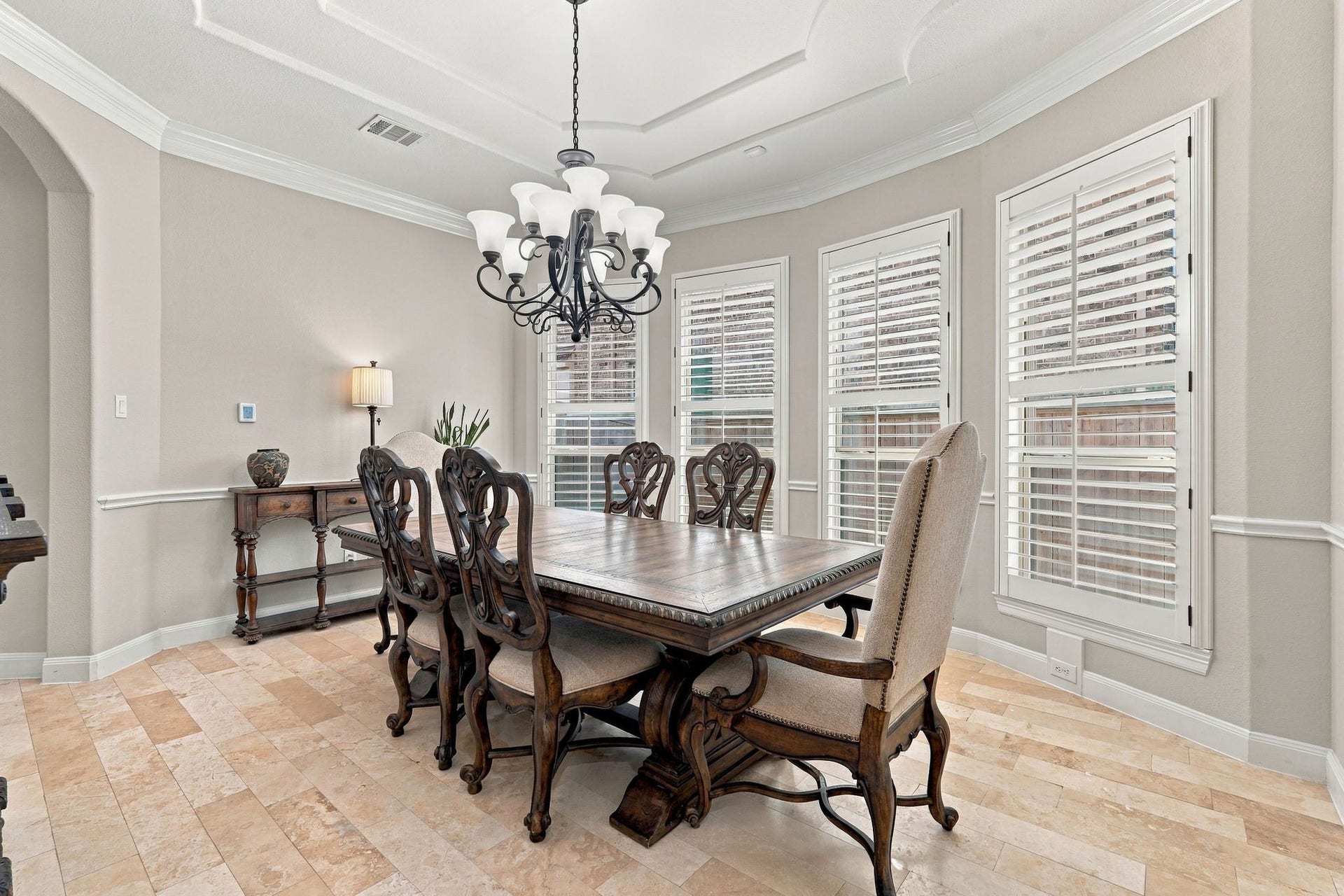 13714 Arcott Bend Drive, Tomball, TX 77377 Beautiful formal dining room featuring an elegant tray ceiling, crown molding, chandelier, travertine flooring, and plantation shutters. Large windows provide abundant natural light, creating an inviting space for entertaining and special gatherings.
