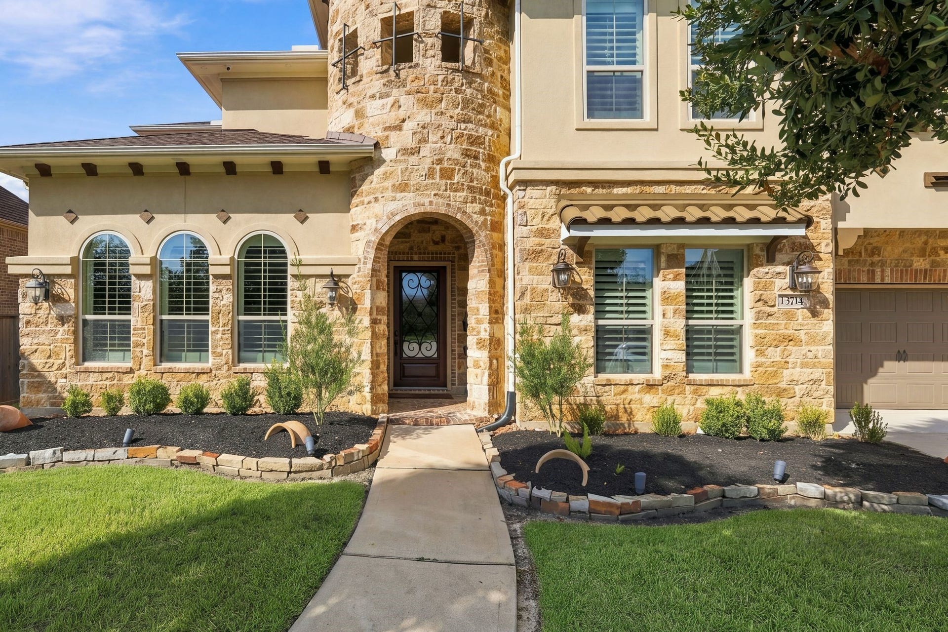 13714 Arcott Bend Drive, Tomball, TX 77377 Impressive front entry featuring a distinctive natural stone turret, beautiful arched windows, decorative wrought-iron glass front door, and elegant architectural details. Professionally maintained landscaping enhances the exceptional curb appeal of this luxury home in gated Wildwood at Northpointe.