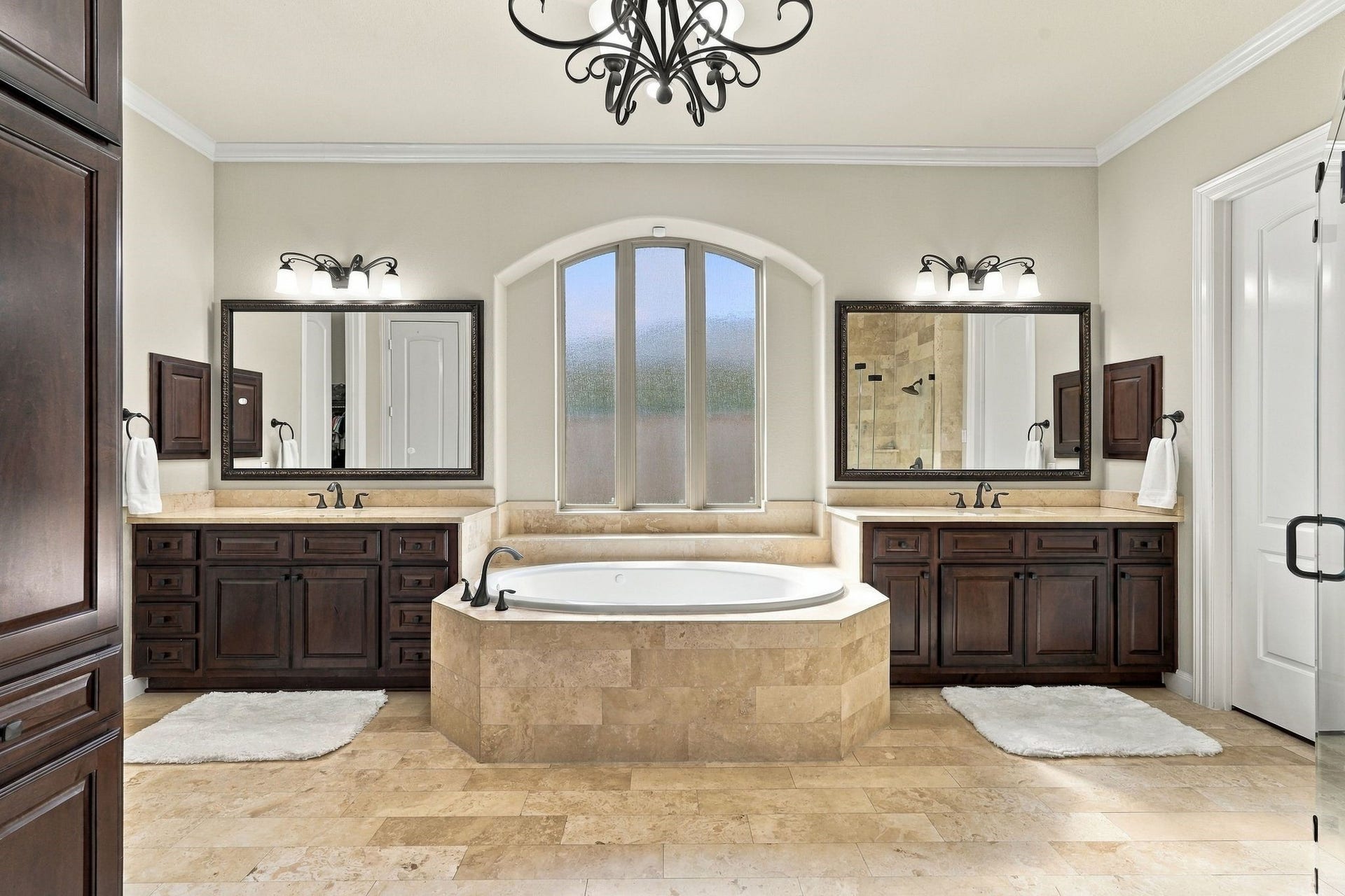13714 Arcott Bend Drive, Tomball, TX 77377 Spa-inspired primary bathroom exudes timeless luxury with a stunning soaking tub framed by an elegant arched window, dual granite-topped vanities with rich wood cabinetry, and beautiful travertine flooring. The spacious, thoughtfully designed retreat offers an exceptional blend of elegance, comfort, and relaxation.