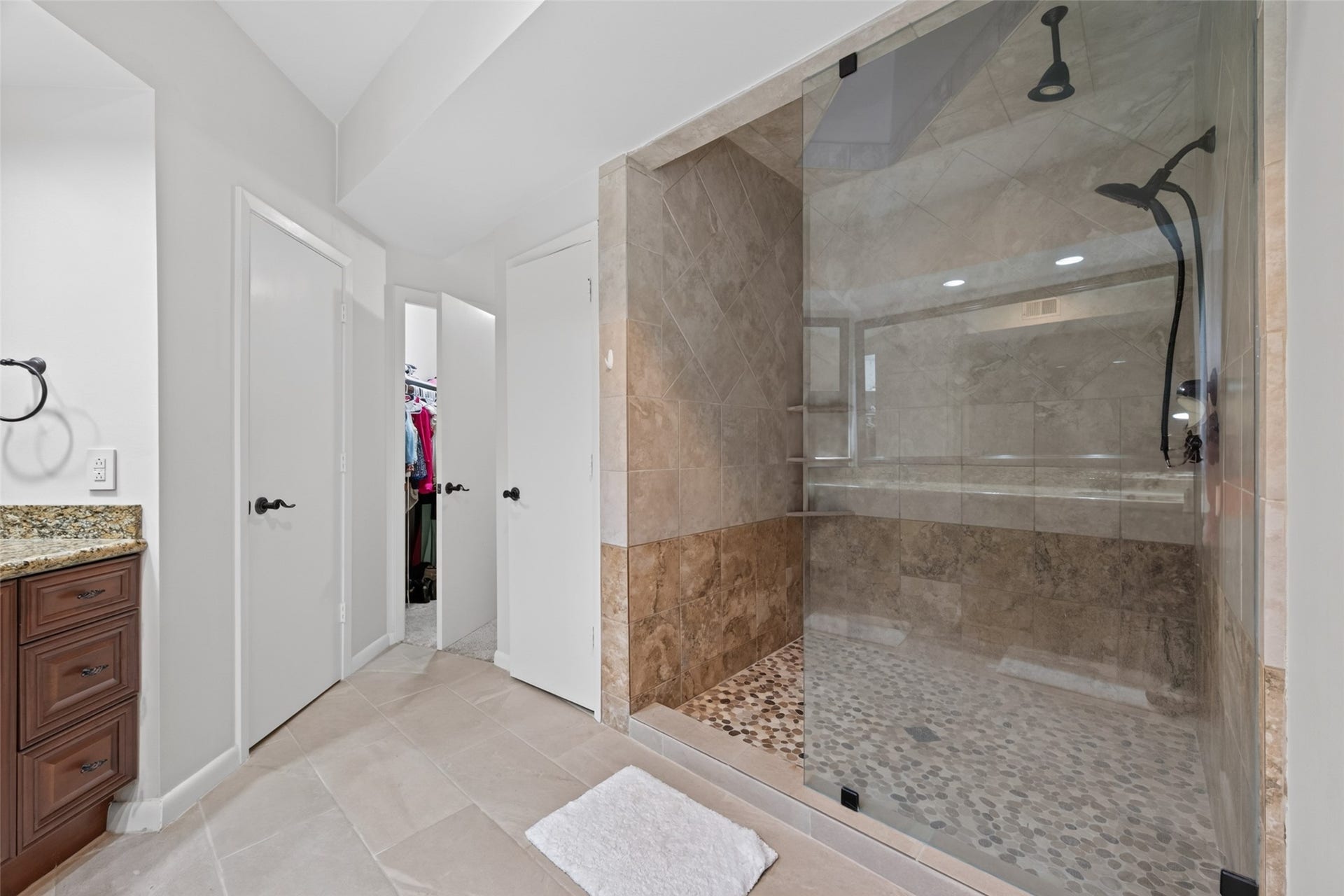This bathroom features a spacious, glass-enclosed shower with stone tiles, a granite countertop vanity, and access to a walk-in closet.