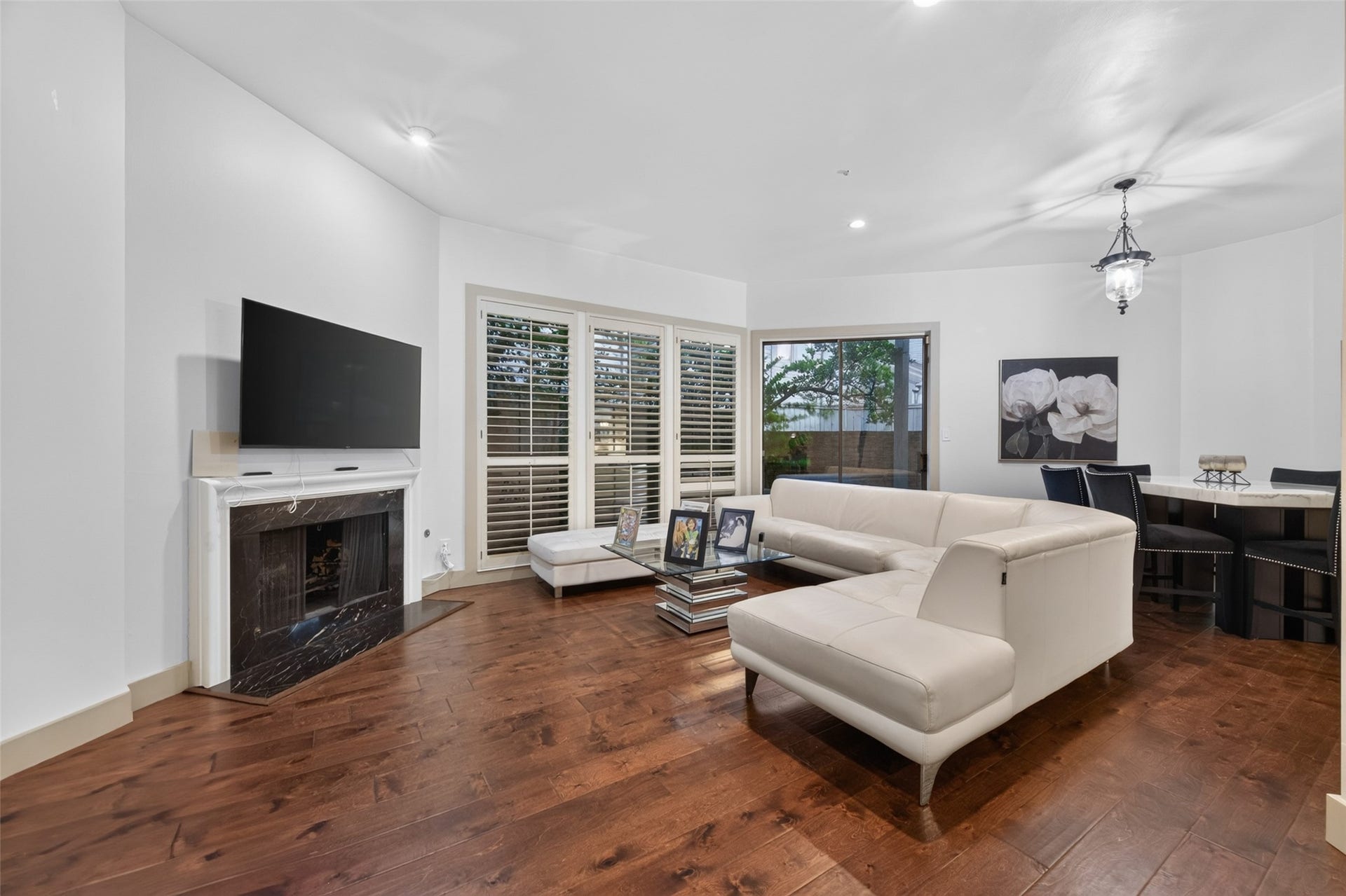 This spacious living area has a modern design with engineer wood floors, a cozy fireplace, and large windows for natural light. It features a comfortable white sectional sofa and a stylish dining area, perfect for entertaining or relaxing.